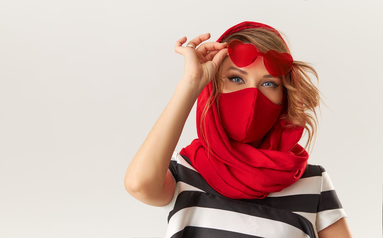 Woman in trendy fashion outfit during quarantine of coronavirus outbreak. Model in protective stylish red face mask and heart shape sunglasses on white background