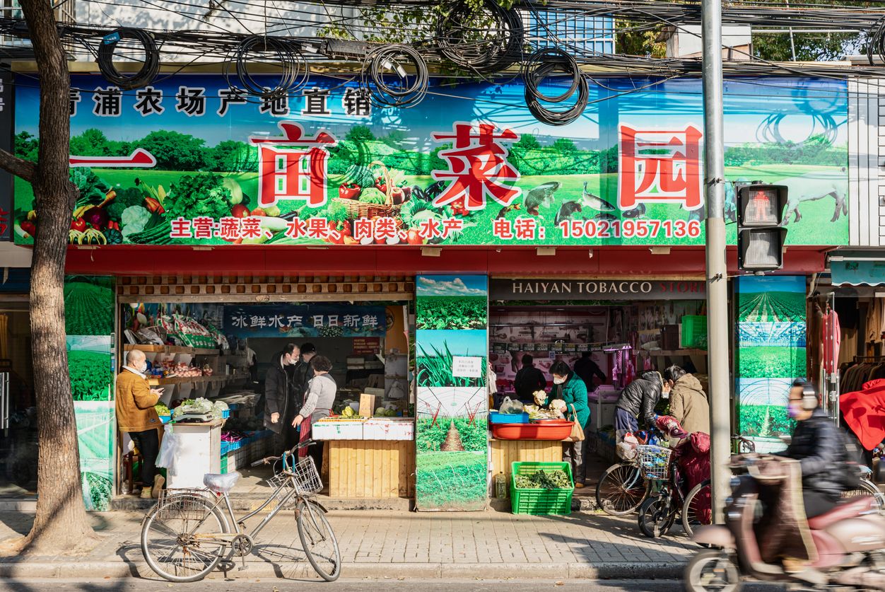 Shanghai, China - March 14, 2020: View of a vegetable, meat and food store on a street in historic old-town Jiangwanzhen, Hongkou district. People wear face masks.