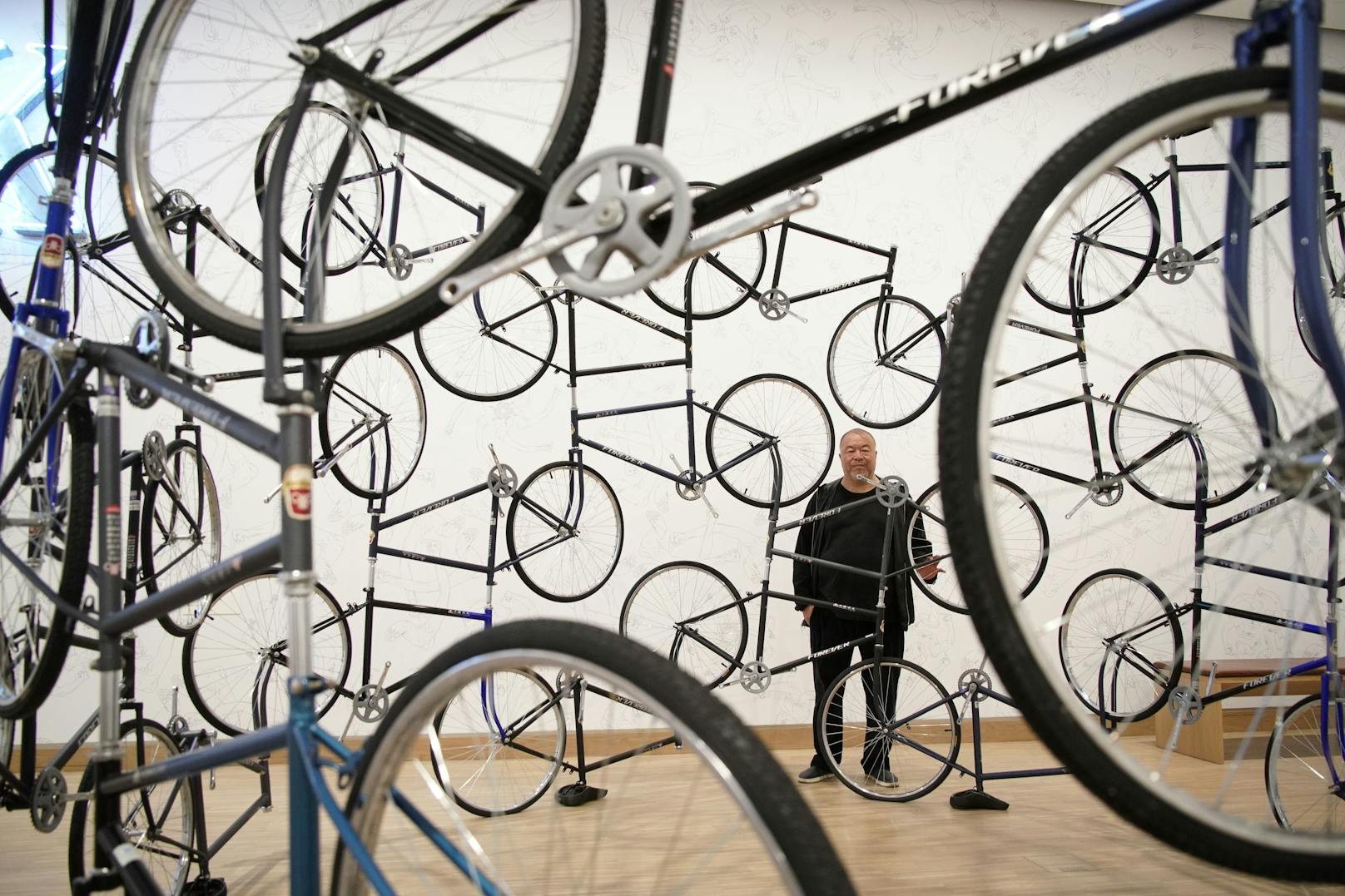 Ai Weiwei hinter seiner Installation "Forever Bicycles, 2003".&nbsp;Ai montiert die Fahrräder so aneinander, dass sie nicht mehr funktionstüchtig sind, ohne Lenker, Pedale und Ketten, teils ohne Sattel. Er spielt damit auf die chinesische Bevölkerung an, auf deren Synchronisierung und Uniformierung, deren Zusammenspiel als Kollektiv, das jedoch dem Einzelnen kaum Bewegungsfreiheit ermöglicht.