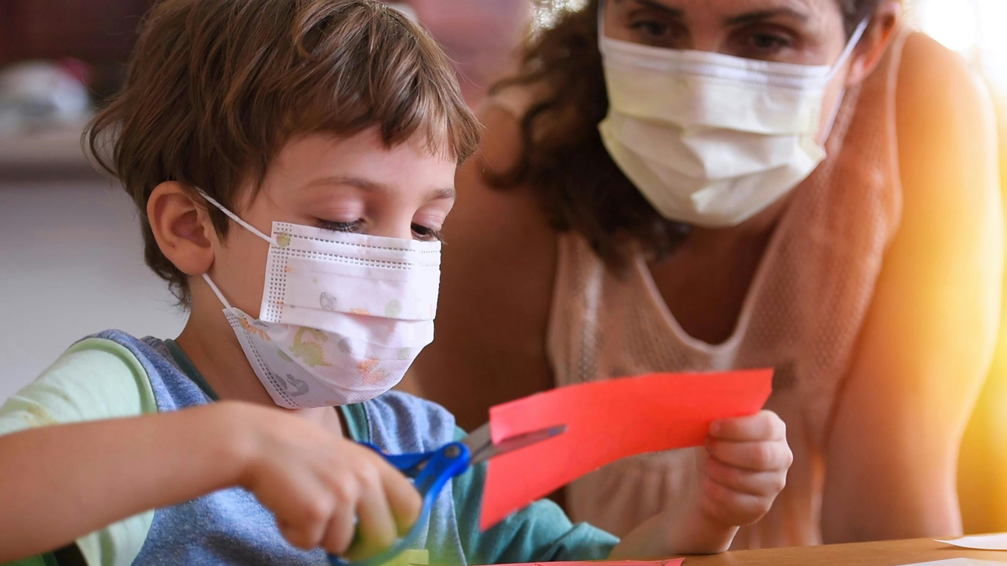 Caucasian Little boy at pre school classroom with his teacher, both wearing a protective face mask (picture taken in a real US classroom)