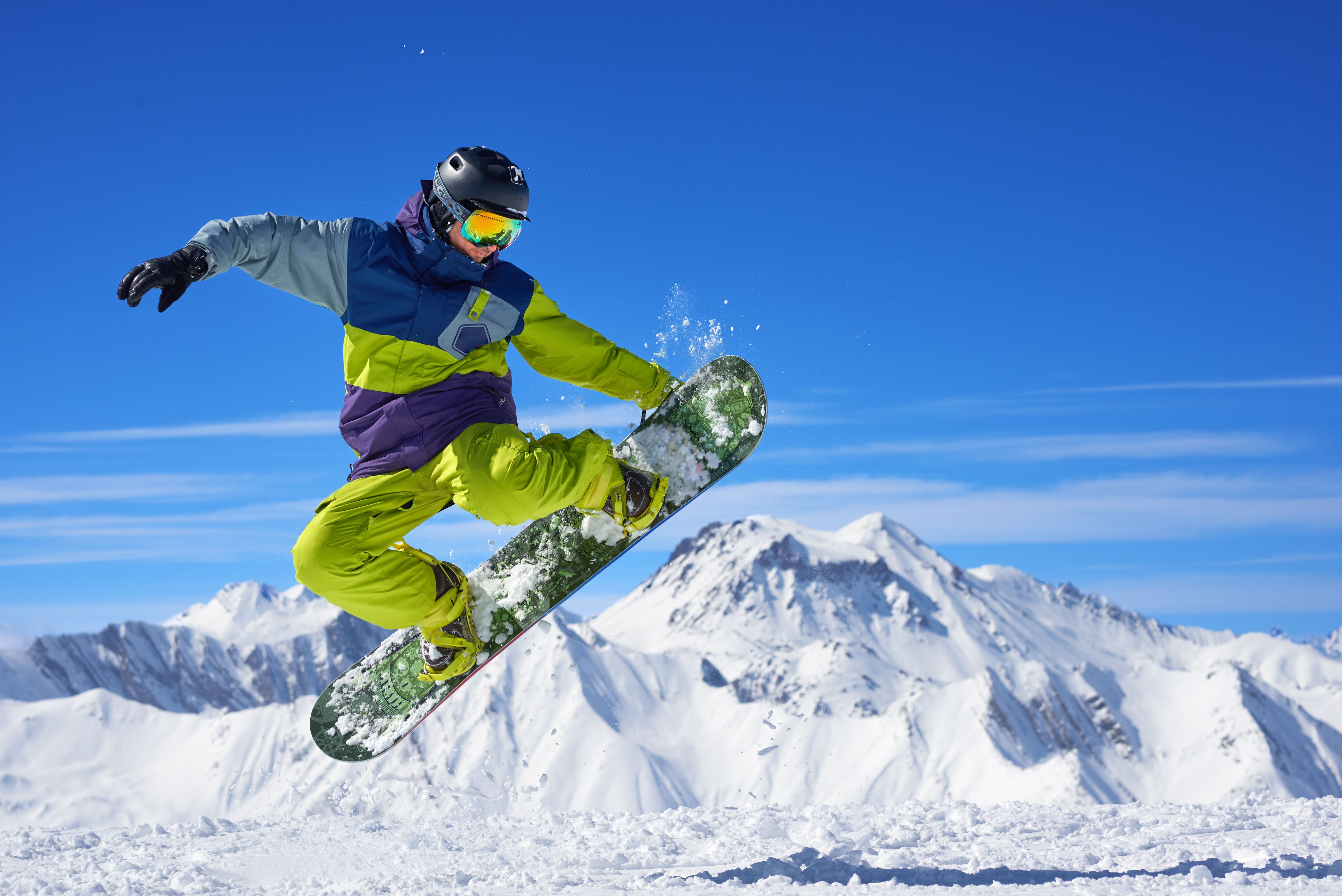 Snowboarder in bright sportswear doing trick against of beautiful mountains