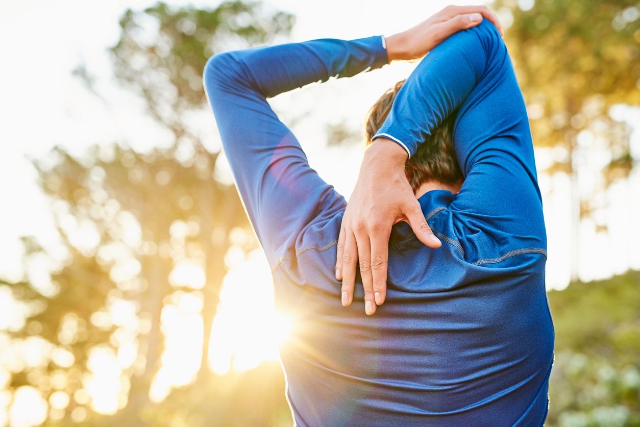Rear view of young man stretching arm and shoulder outdoors. Male athlete is warming up before jogging. He is representing healthy lifestyle.
