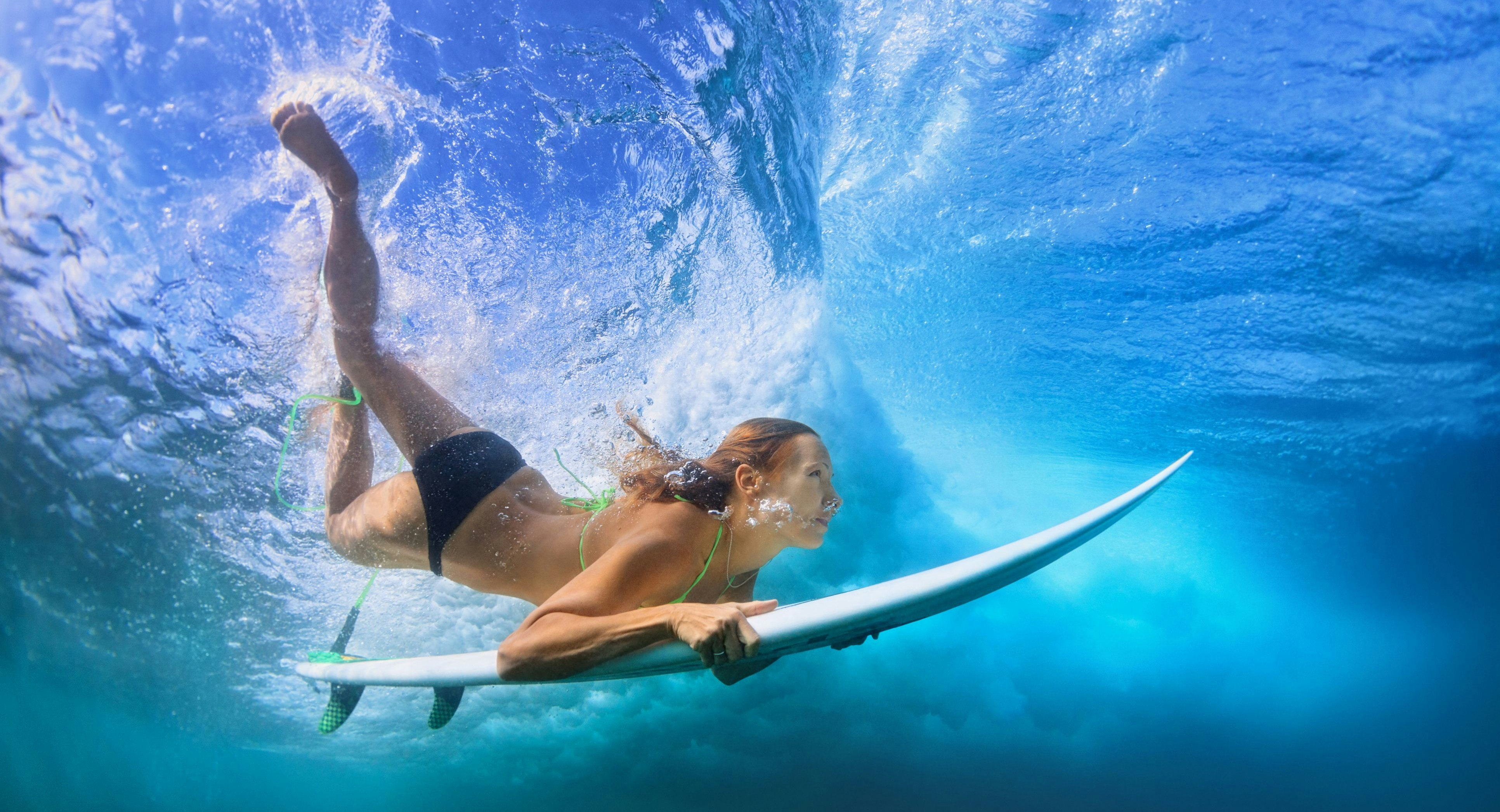 Young active girl in bikini in action - surfer with surf board dive underwater under breaking big ocean wave. Family lifestyle, people water sport adventure camp, beach extreme swim on summer vacation