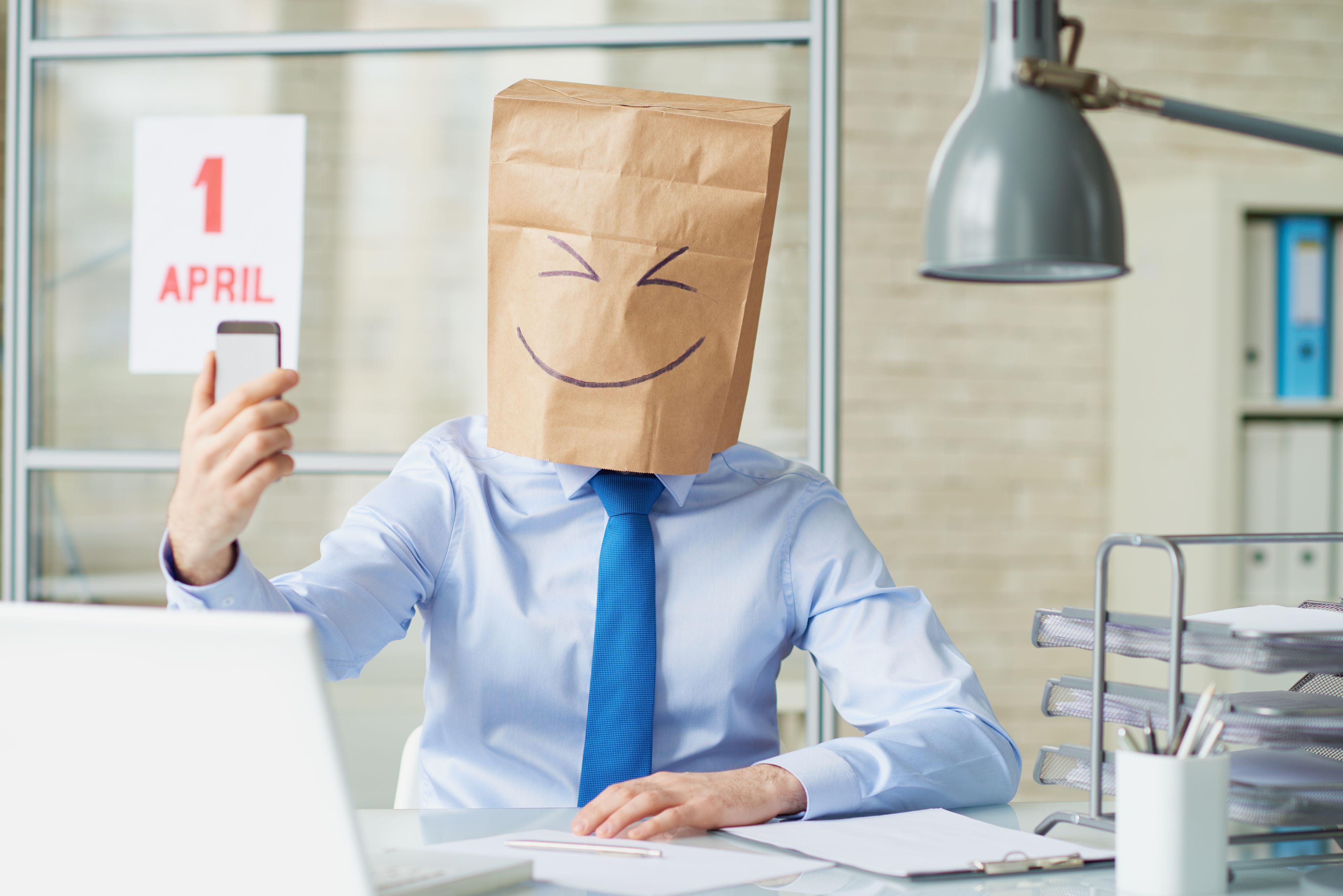 Office worker wearing paper bag taking a selfie with smart phone on April fools day
