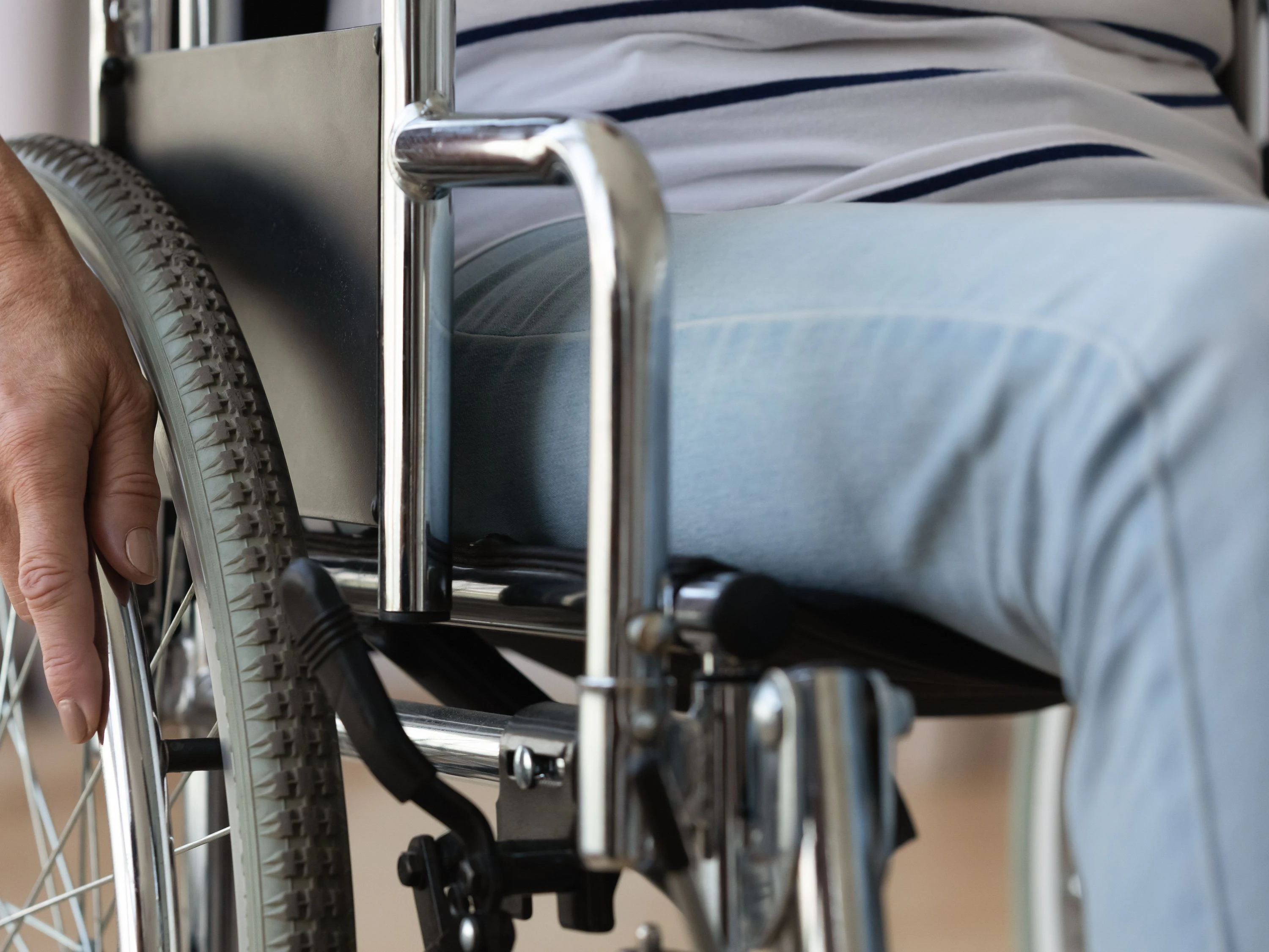 Close up disabled older woman sitting in wheelchair, touching wheels, moving at home alone, rehabilitation and recovery after injury, medical equipment, disability and healthcare