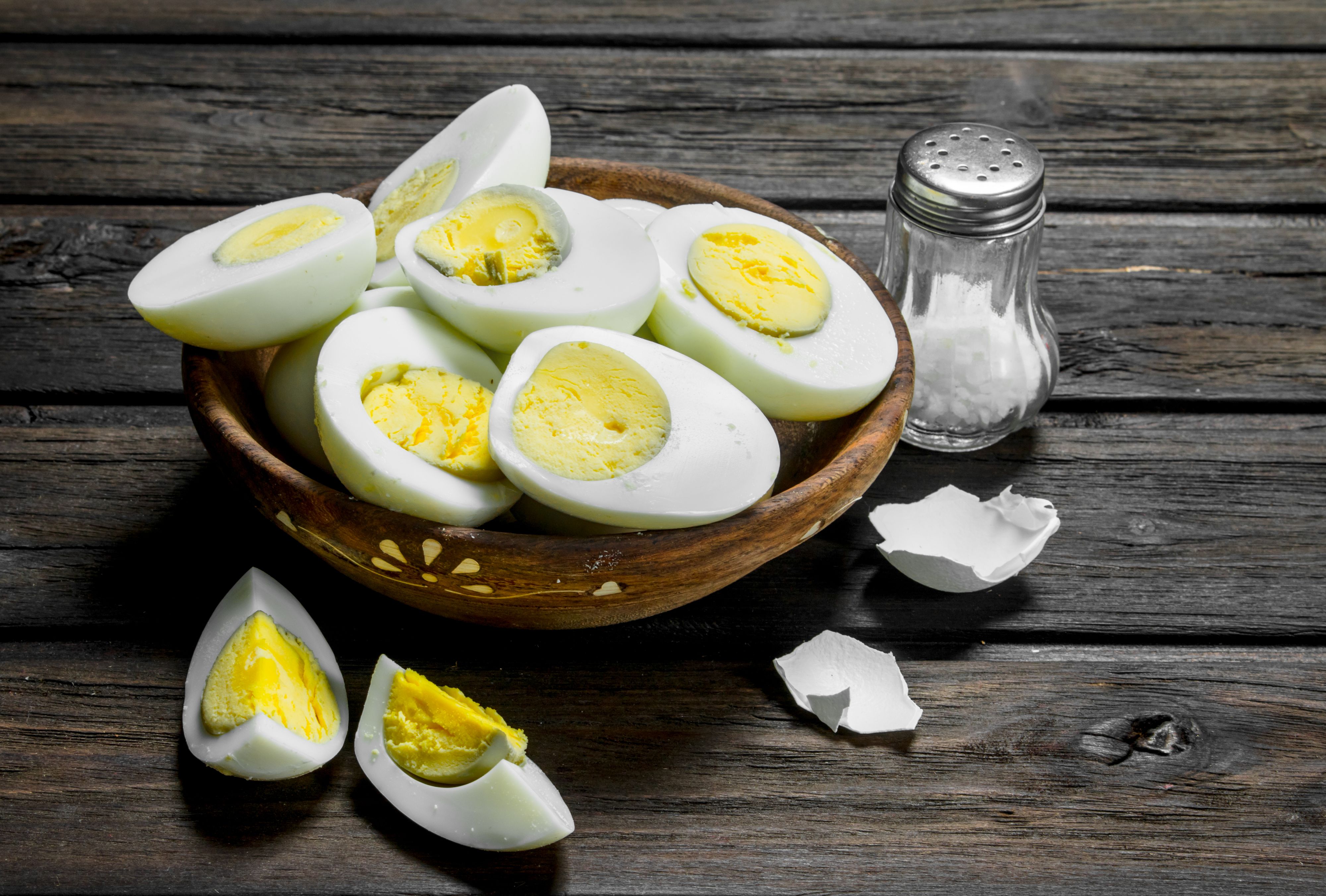Boiled eggs in bowl with salt. On a wooden background.