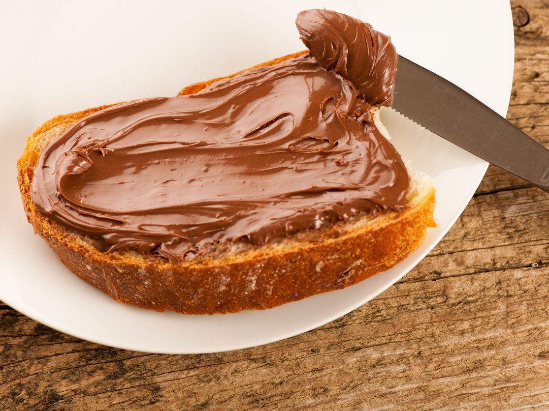 Slice of bread with sweet chocolate nougat spread on white plate.