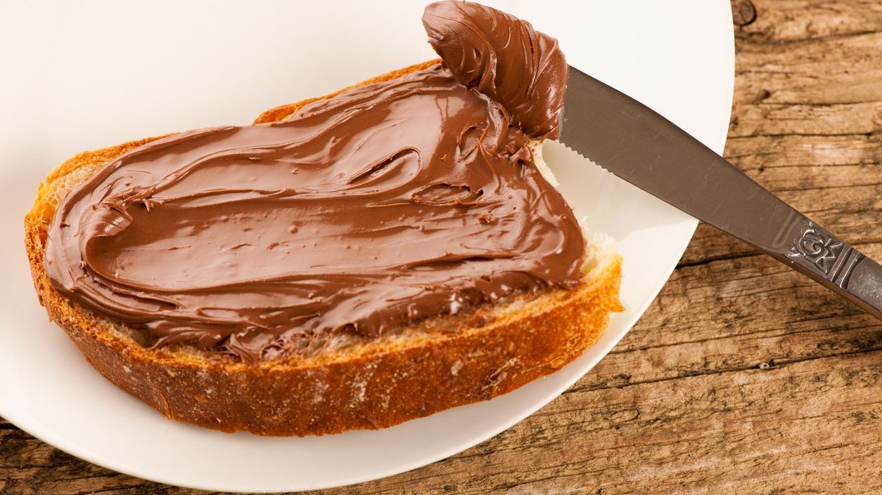 Slice of bread with sweet chocolate nougat spread on white plate.