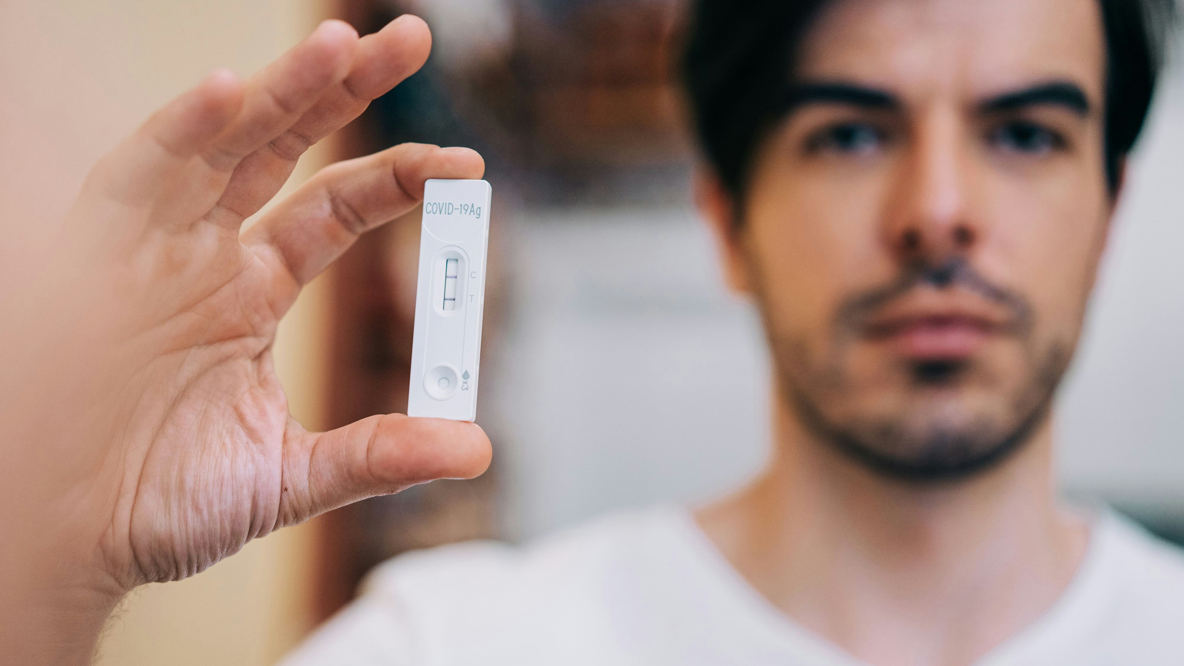 Close-up shot of man's hand holding a positive test device. Young man showing his positive Coronavirus/Covid-19 rapid test. Focus is on the test.