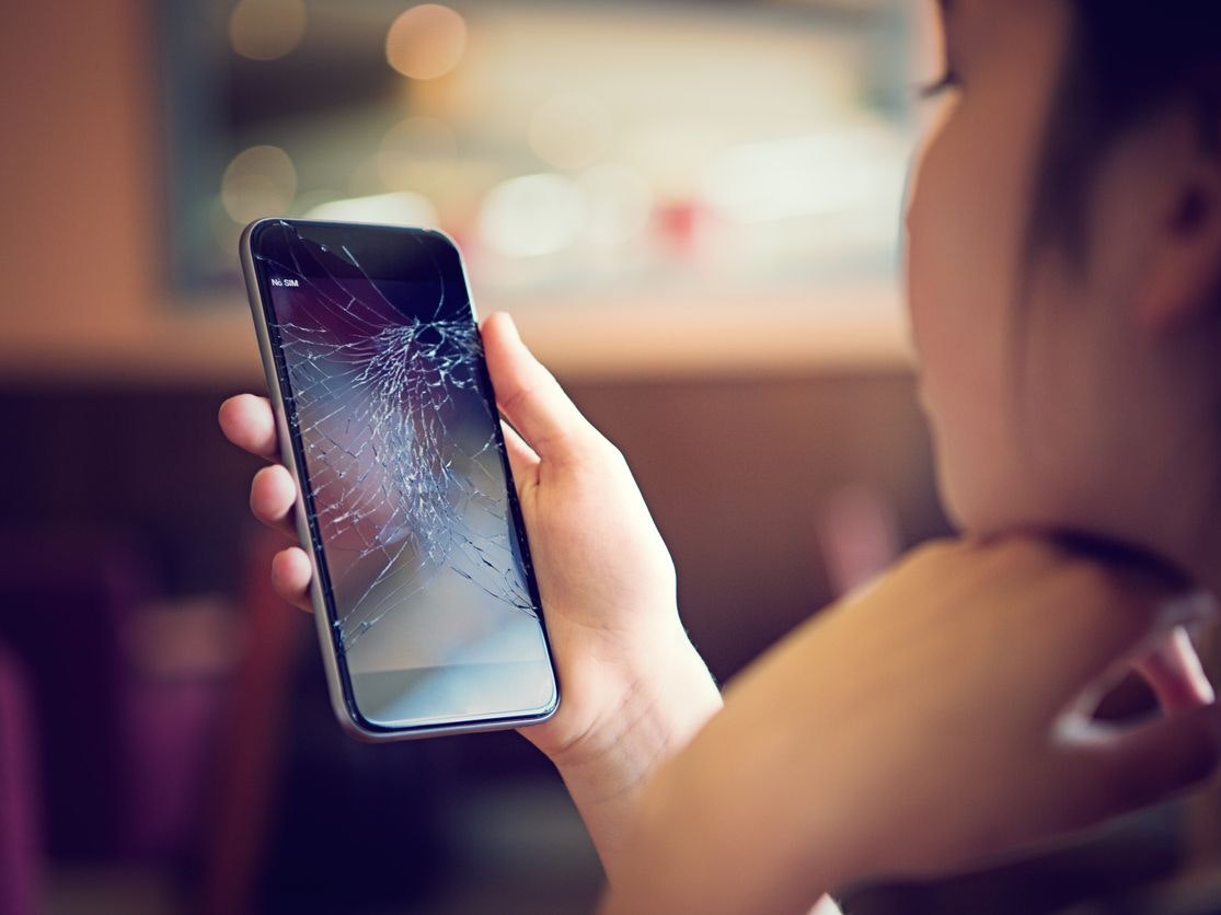 Young girl is watching her broken mobile phone after falling down.