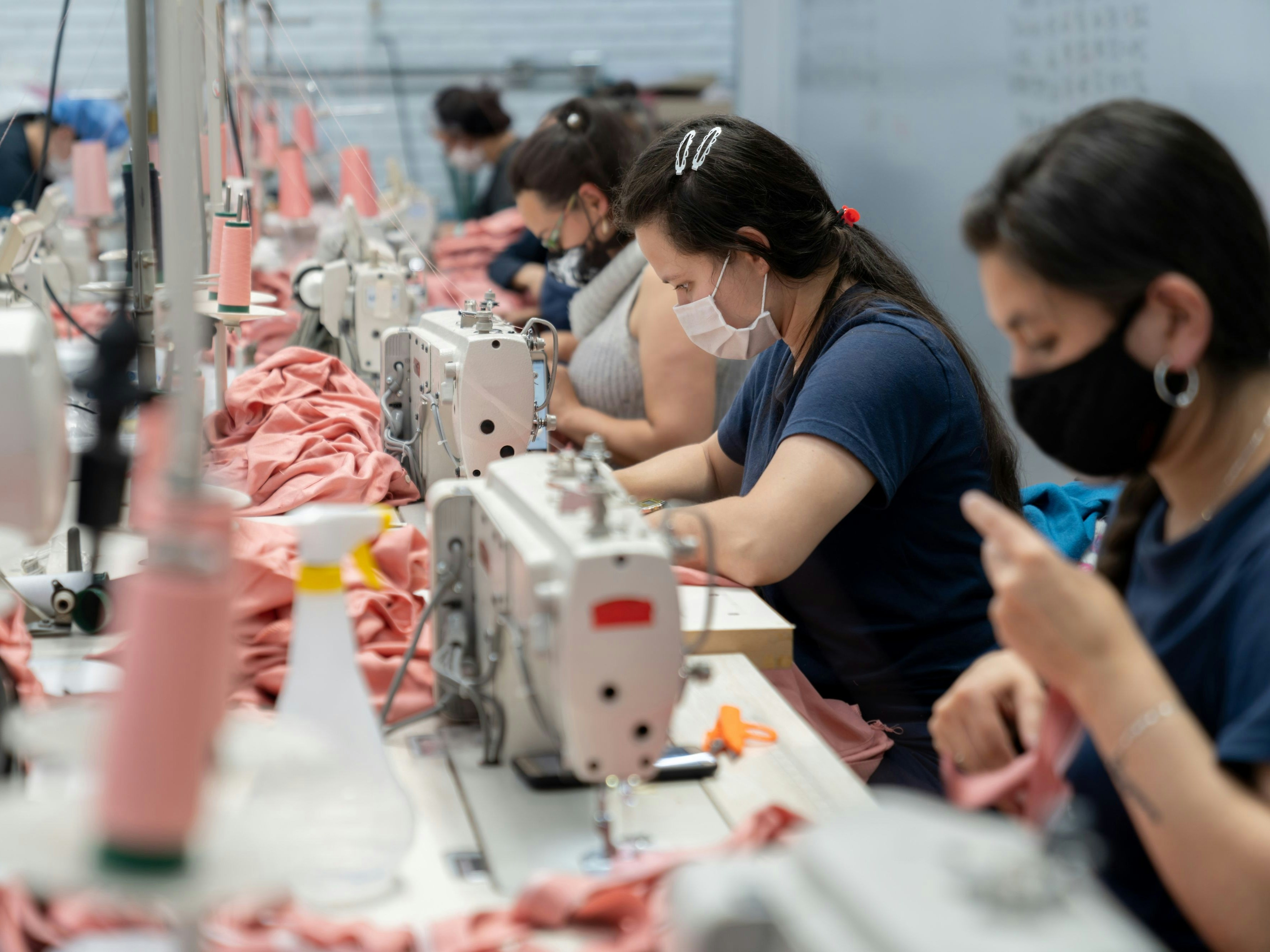 Group of Latin American women working at a textile factory wearing a facemask while sewing clothes during the COVID-19 pandemic