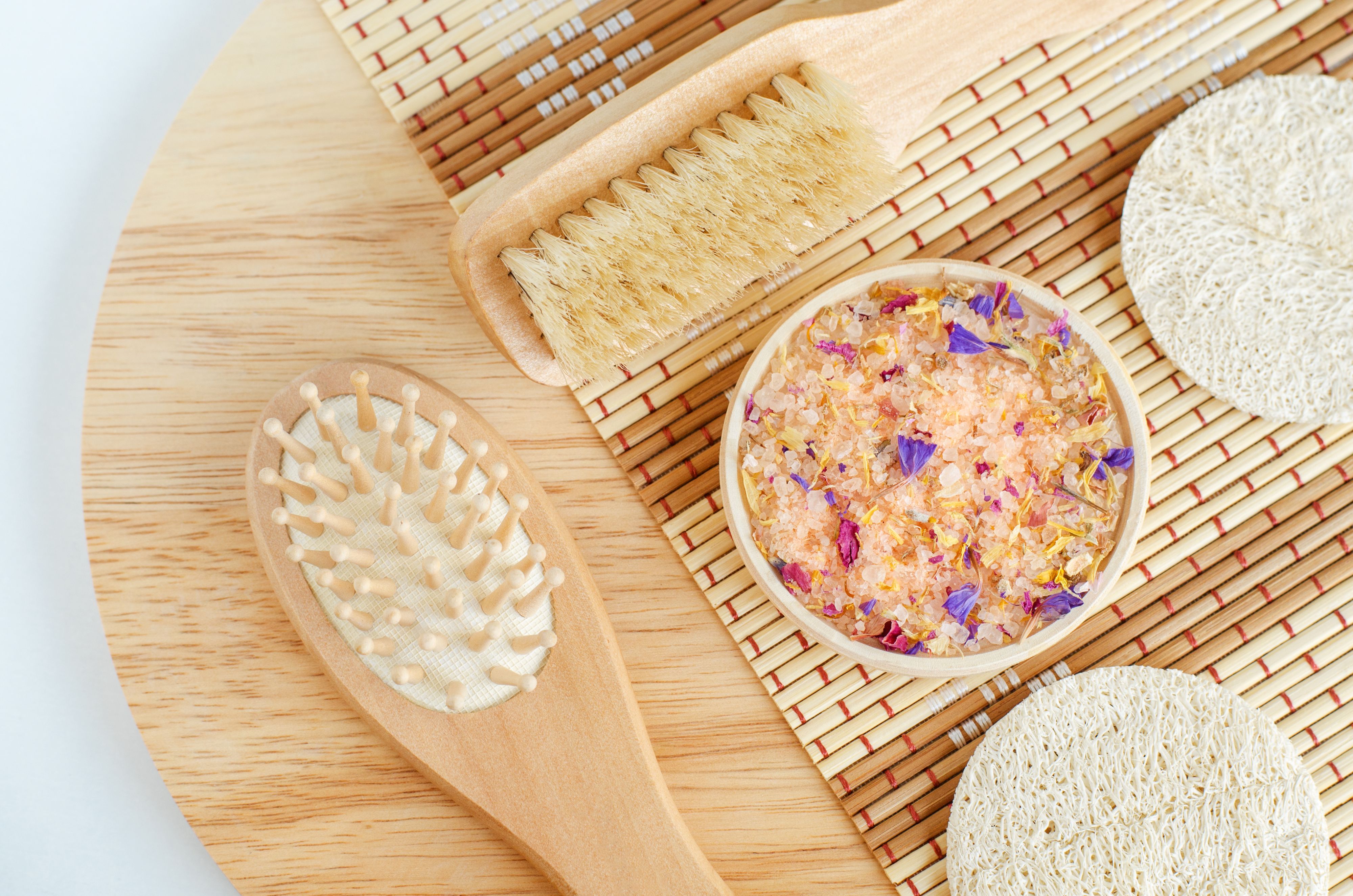 Pink floral bath salts, loofah sponge, wooden hairbrush and massage body brush. Natural spa, beauty treatment, zero waste concept. Top view, copy space.