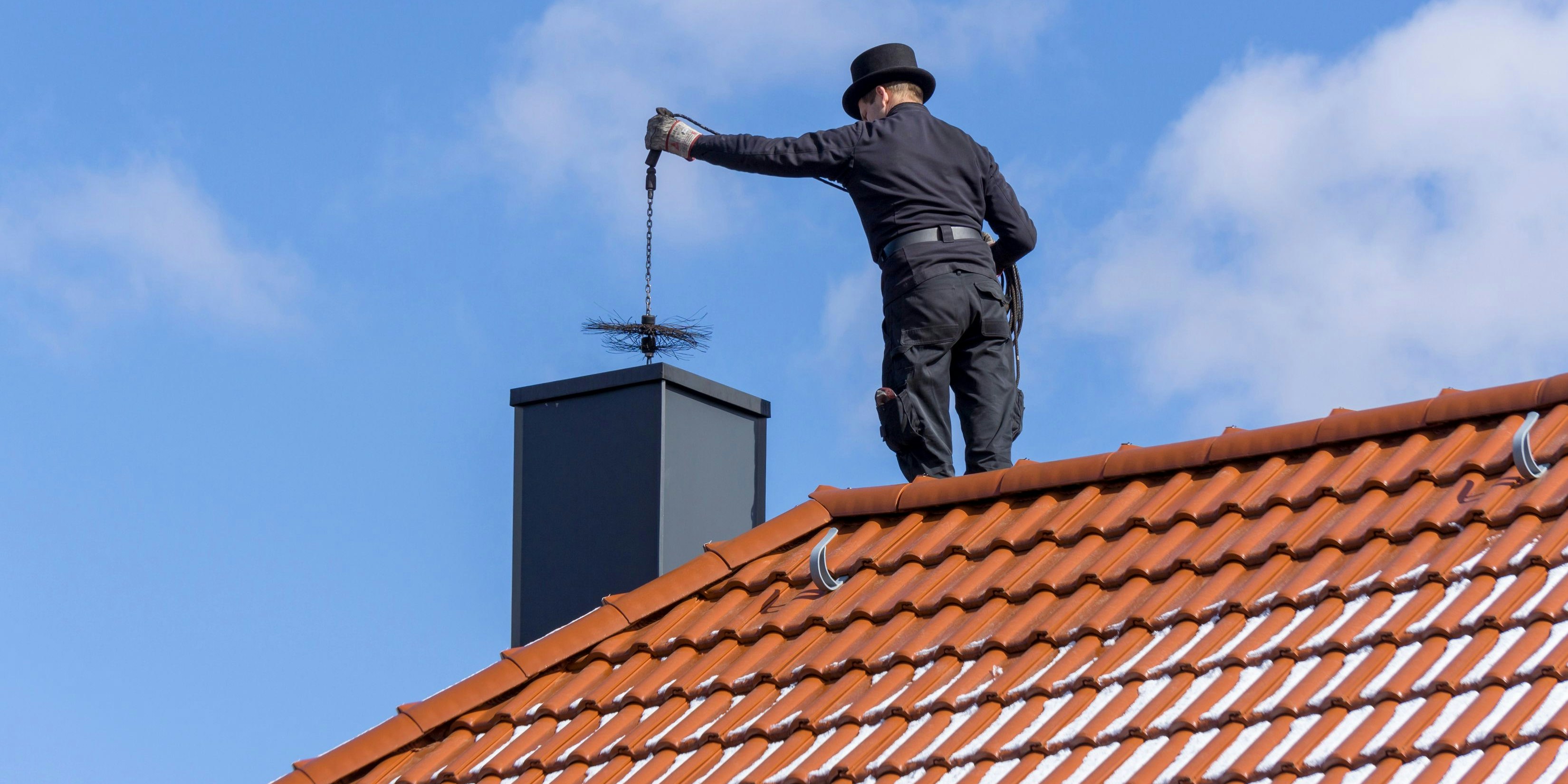 FISCHBACH, GERMANY - March 21 2018: Chimney sweep cleaning a chimney standing on the house roof, lowering equipment down the flue