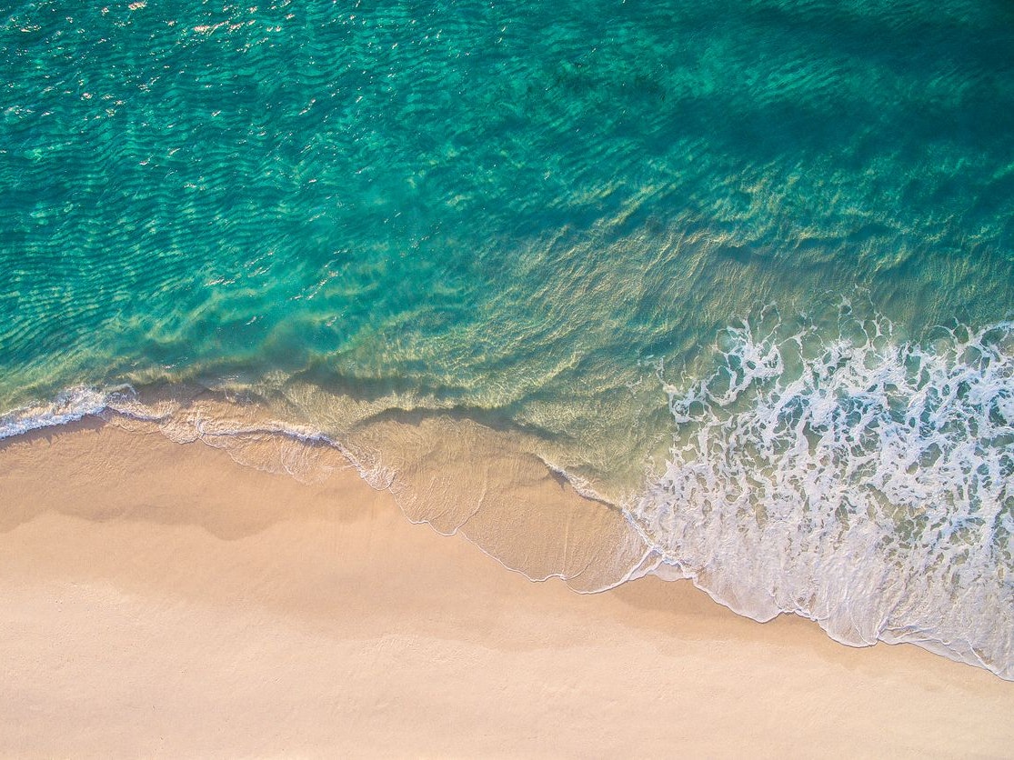 Clean ocean waves breaking on white sand beach with turquoise emerald coloured water. Aerial view. Perfect weather.