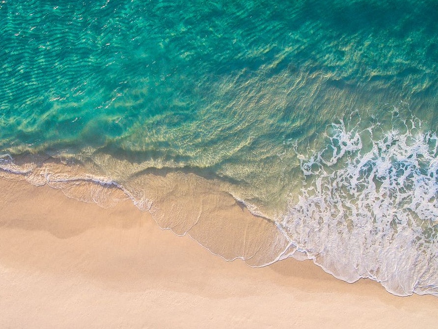 Clean ocean waves breaking on white sand beach with turquoise emerald coloured water. Aerial view. Perfect weather.
