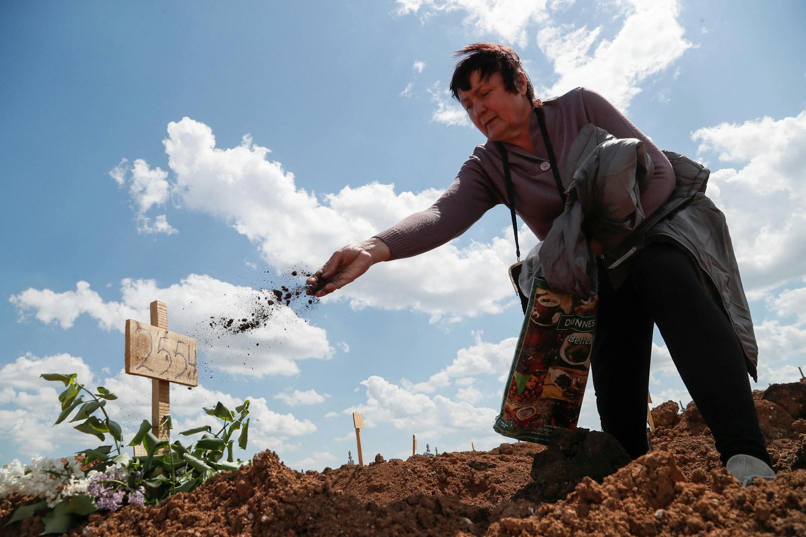 Nadezhda (66) wirft eine Hand voll Erde auf das Grab eines getöteten Familienmitglieds.