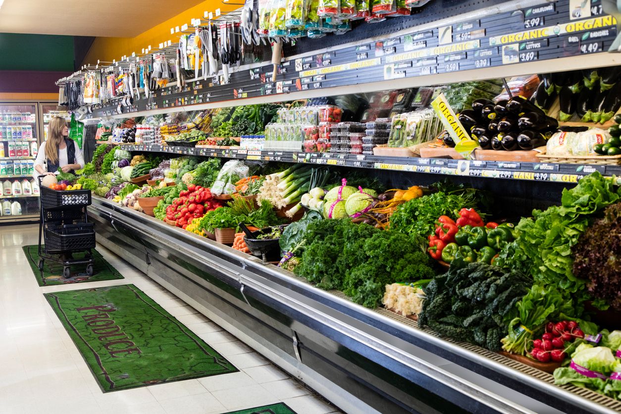 Woman with cart shopping in grocery store in the produce section.
