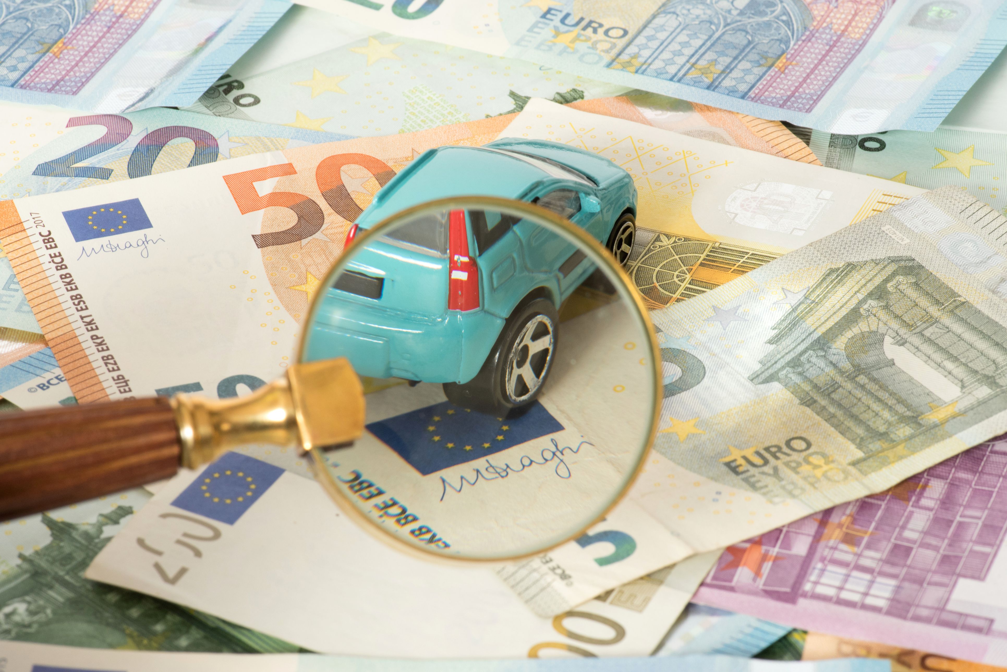 A car, a magnifying glass and many euro banknotes