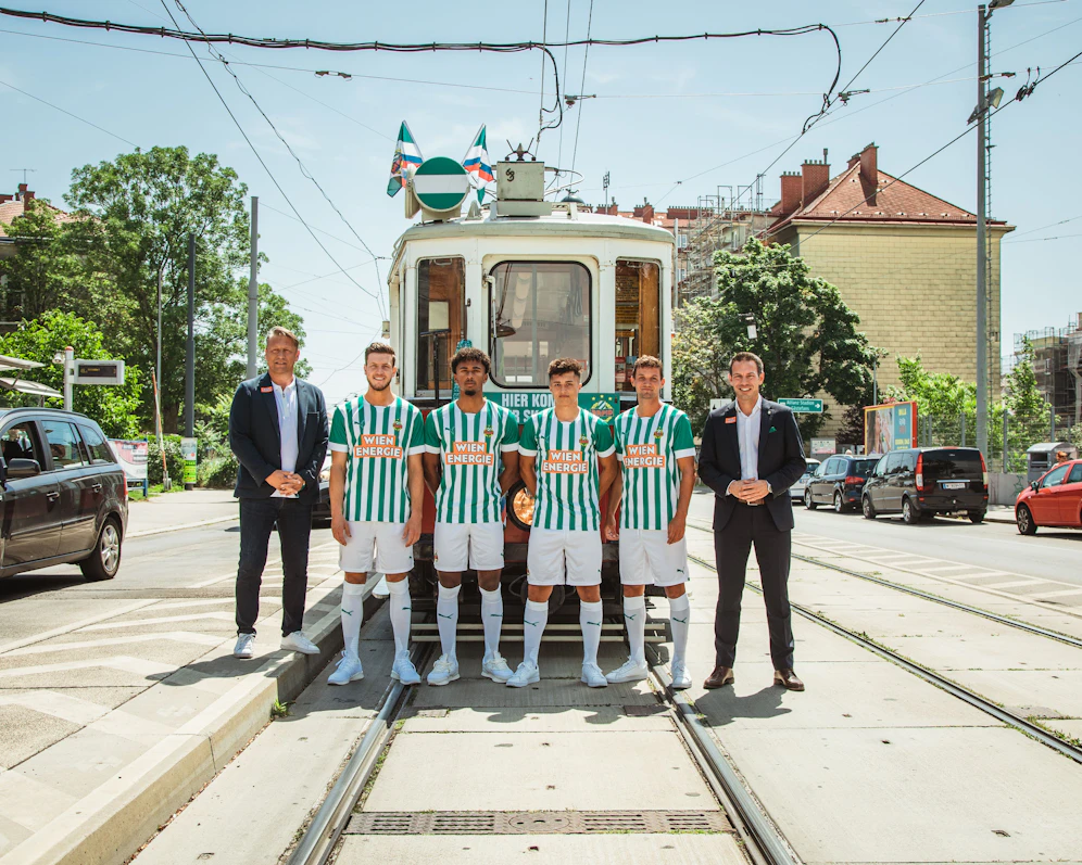 Das neue Rapid-Heimtrikot. Die Spieler posieren gemeinsam mit den Geschäftsführern vor der Straßenbahnlinie 49.