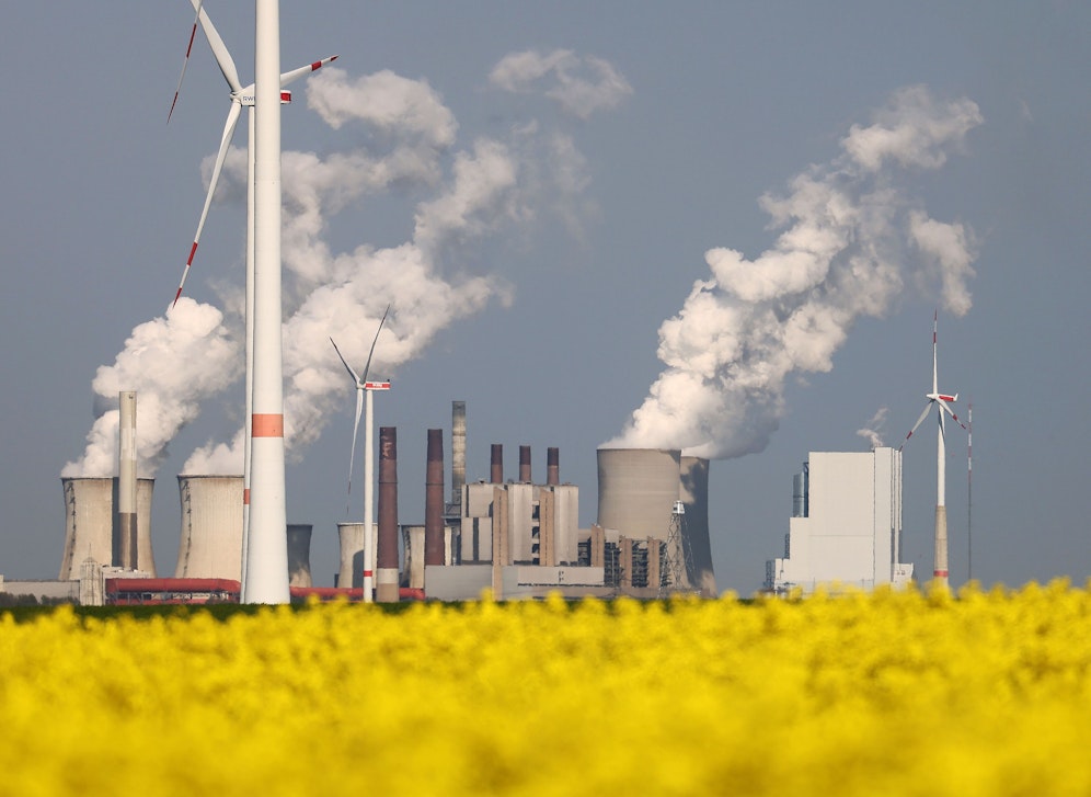 Blick über ein blühendes Rapsfeld und Windturbinen auf das RWE-Braunkohlekraftwerk Neurath, NRW.