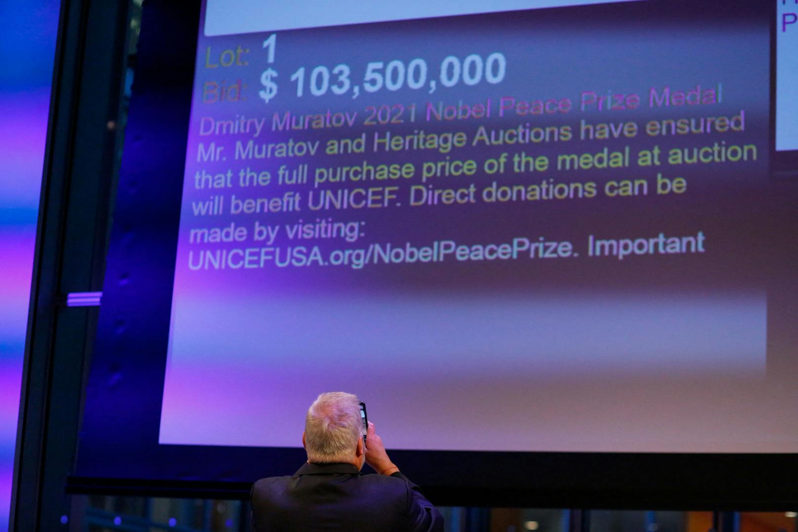 Der russische Journalist Dmitry Muratov macht ein Foto von der Leinwand und kündigt das Gewinnergebot von 103,5 Millionen US-Dollar für den Kauf seiner Friedensnobelpreismedaille am 20. Juni 2022 an. 
