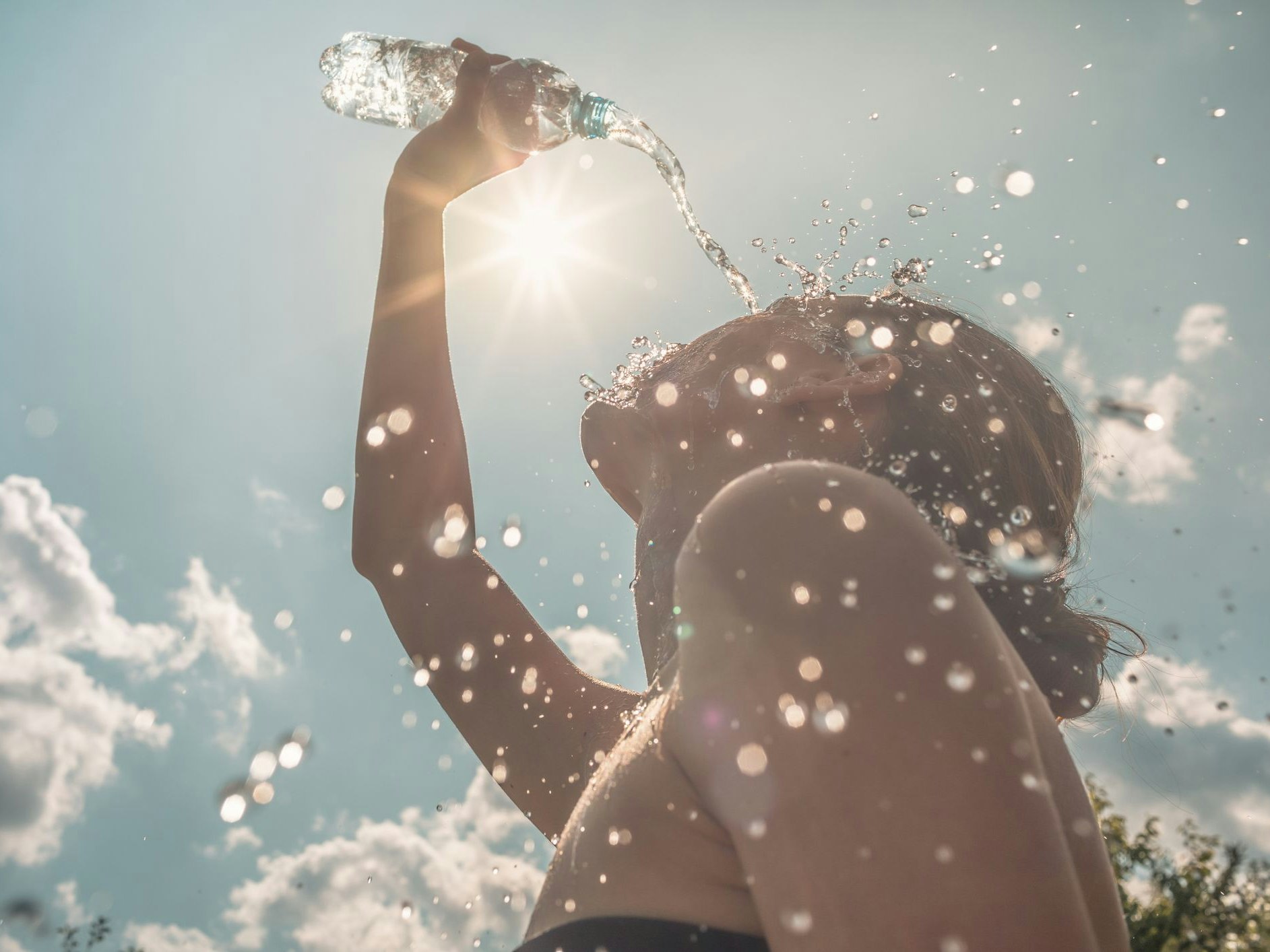 Woman cooling down splashing herself with bottle of water on a hot sunny day.