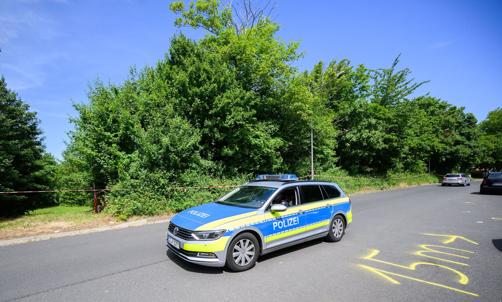 Ein Polizeifahrzeug fährt an dem Tatort auf einer Grünfläche am Hans-Böckler-Ring vorbei.