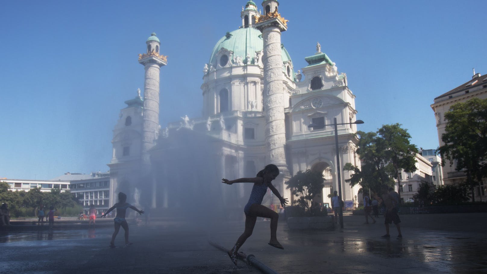 Ein Mädchen springt bei Temperaturen um die 38 Grad Celsius durch eine Wasserfontäne vor der Karlskirche. Archivbild