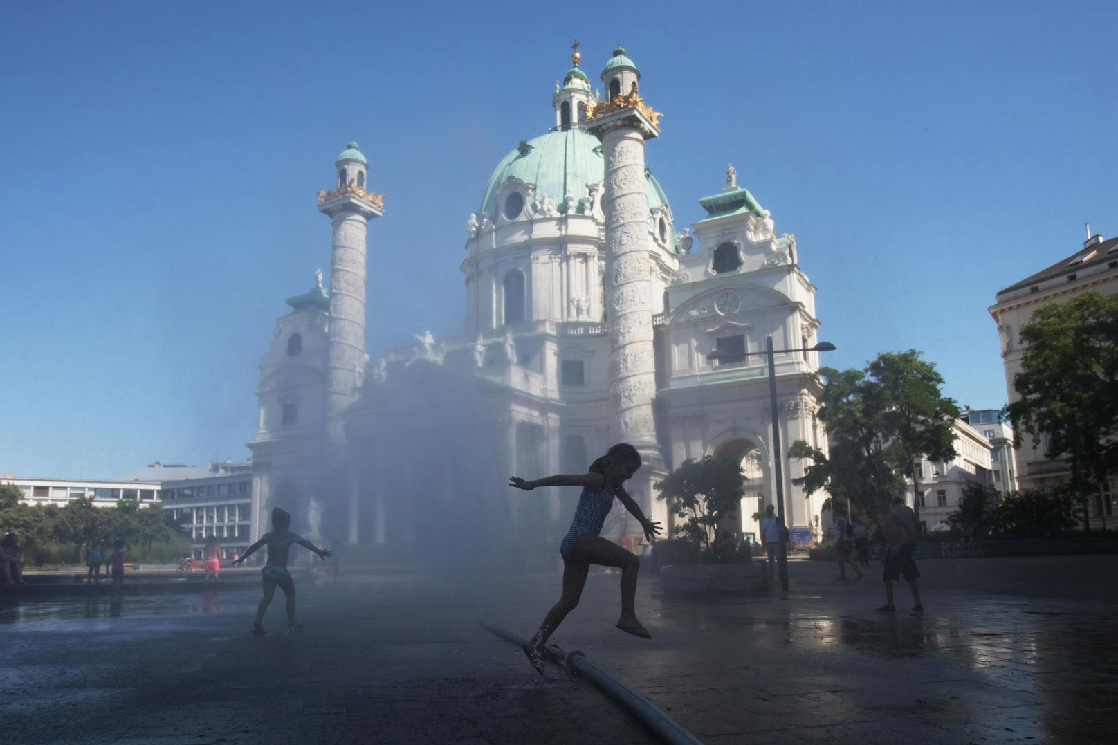 Ein Mädchen springt bei Temperaturen um die 38 Grad Celsius durch eine Wasserfontäne vor der Karlskirche. Archivbild