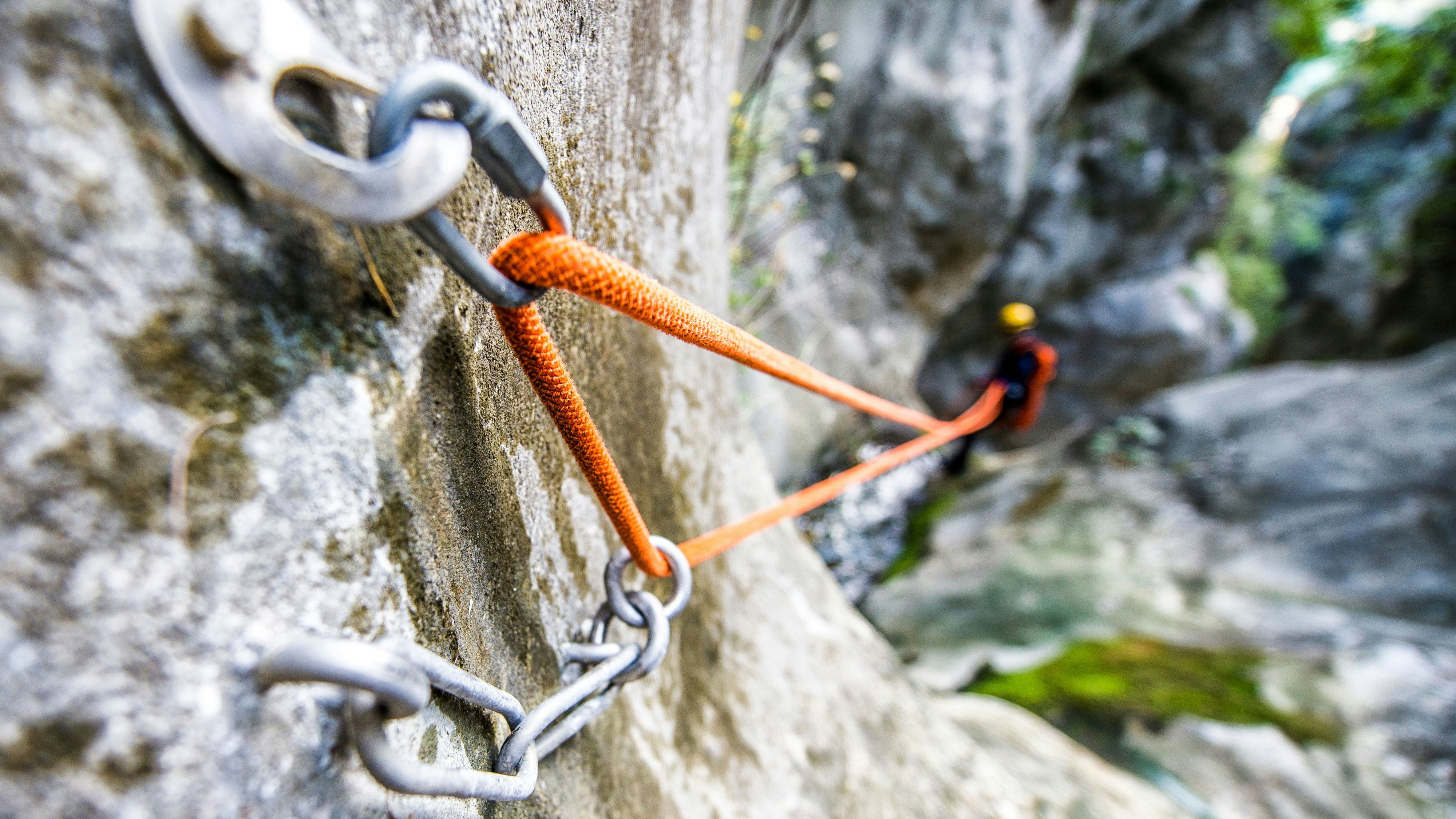 Close up shot of rope security system attached to the rock itself in the canyon. Man is visible in the background while rappeling.