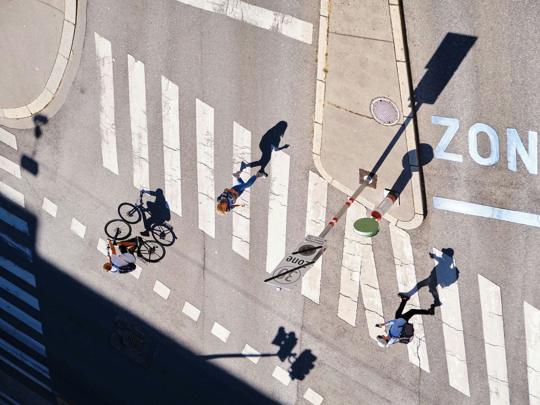 Vienna, Austria - September 13, 2019: Long shadows of people walking and biking at an intersection - aerial view.