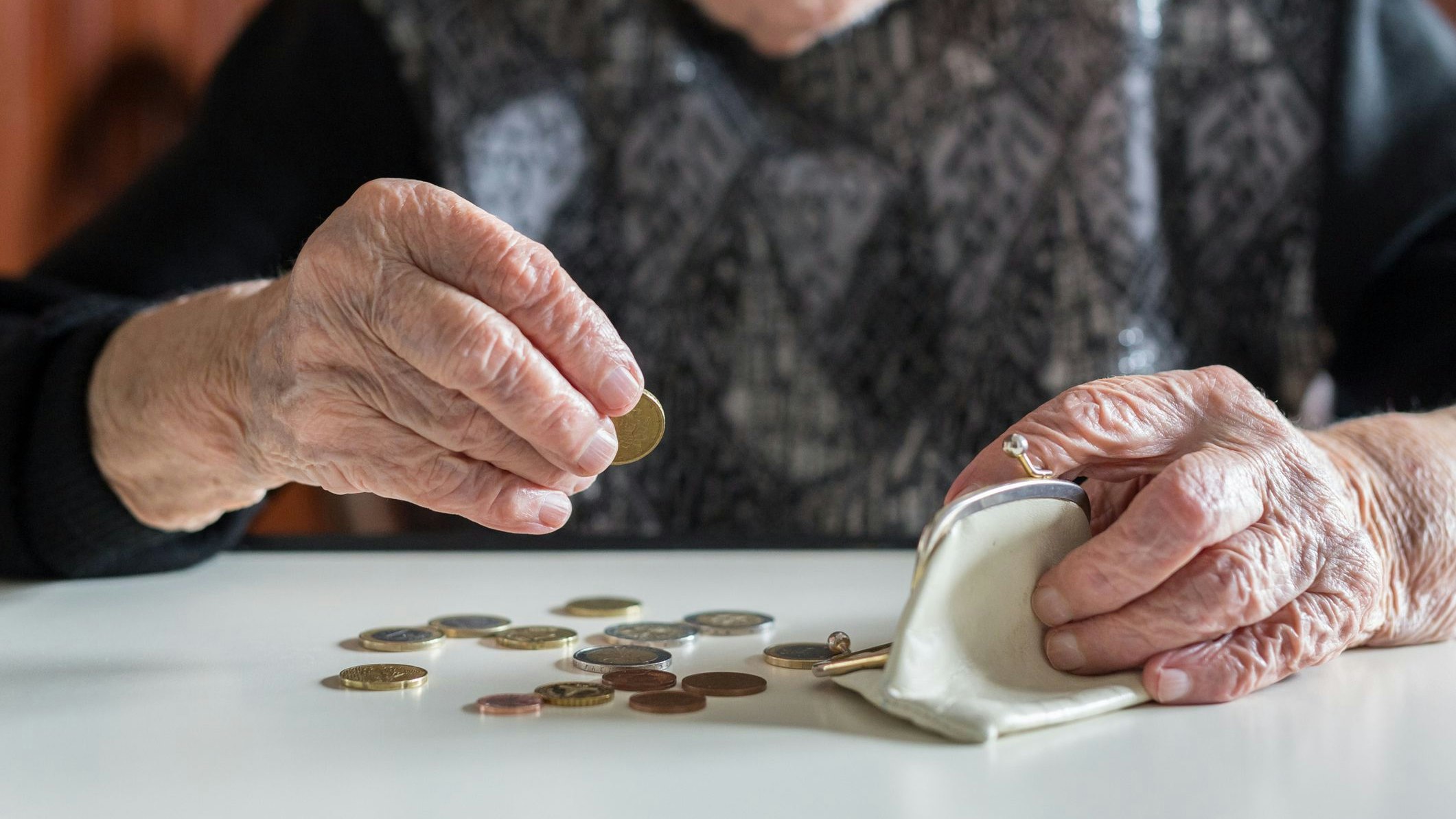 Elderly 95 years old woman sitting miserably at the table at home and counting remaining coins from the pension in her wallet after paying the bills.