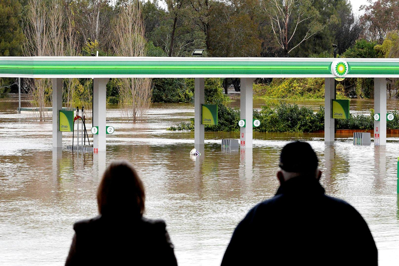 Menschen stehen am 3. Juli 2022 neben einer überschwemmten Tankstelle im Vorort Camden in Sydney.