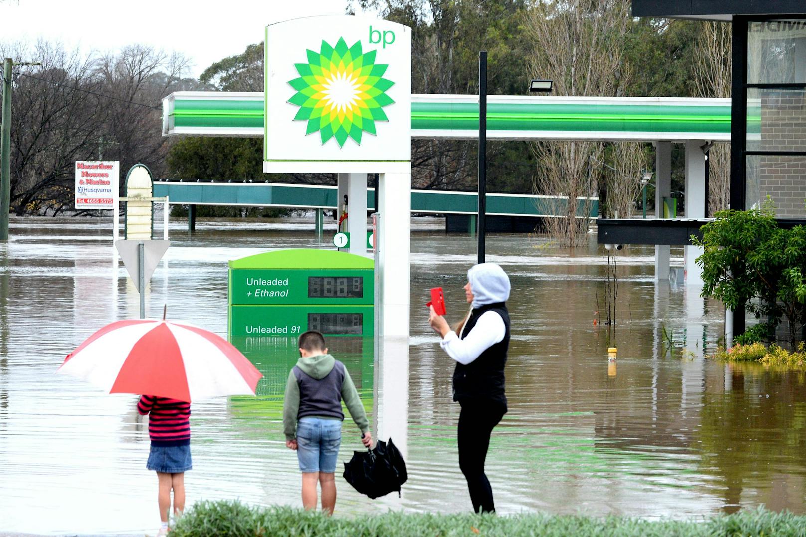 Menschen stehen am 3. Juli 2022 neben einer überschwemmten Tankstelle im Vorort Camden in Sydney, die von sintflutartigen Regenfällen heimgesucht wurde.