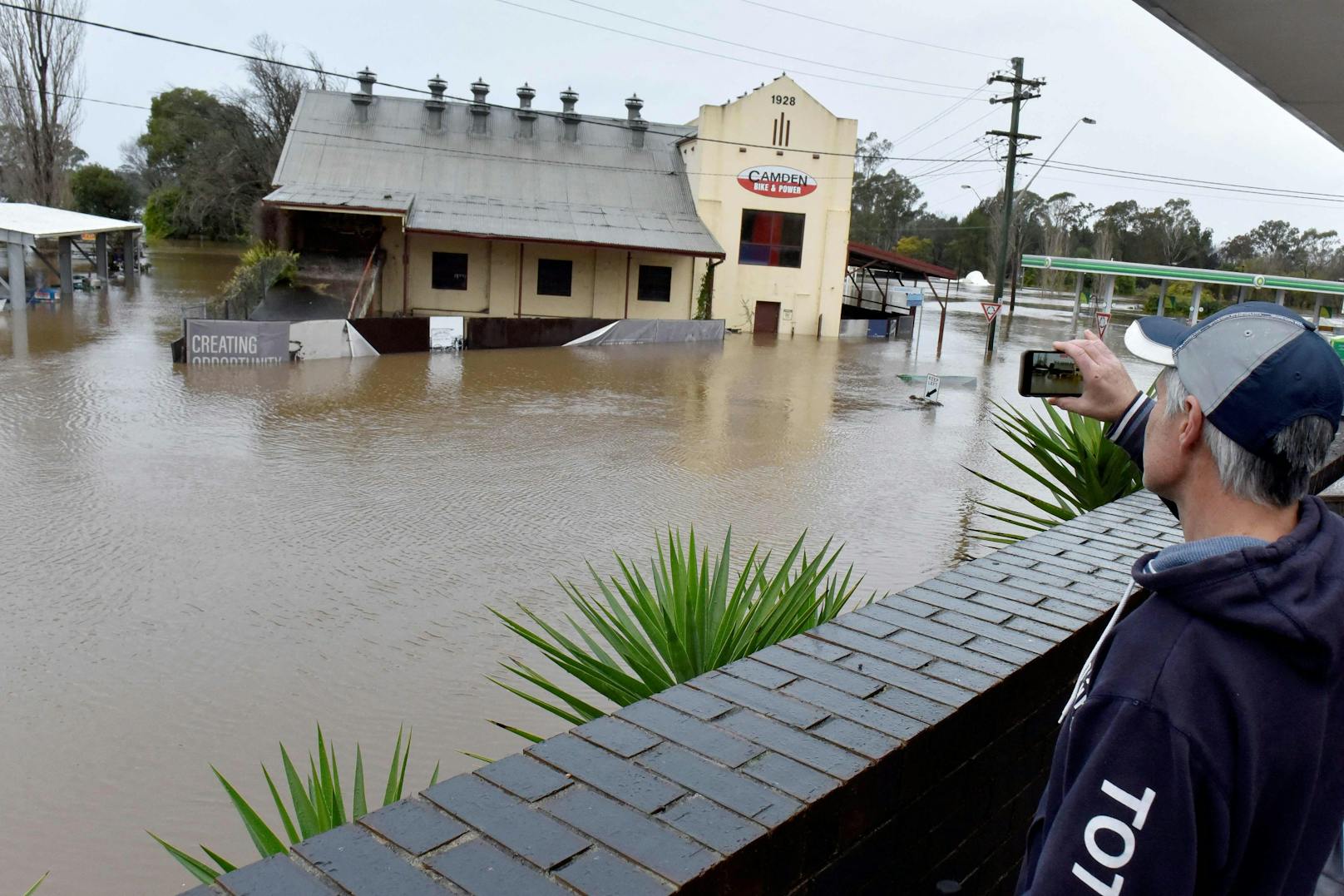 Ein Mann filmt am 3. Juli 2022 überschwemmte Straßen im Vorort Camden von Sydney.
