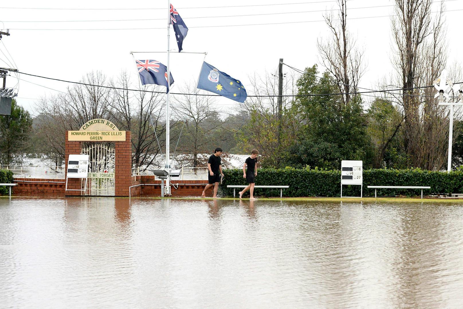 Anwohner bahnen sich am 3. Juli 2022 im Vorort Camden in Sydney einen Weg durch überschwemmte Straßen, die durch sintflutartige Regenfälle entstanden sind.