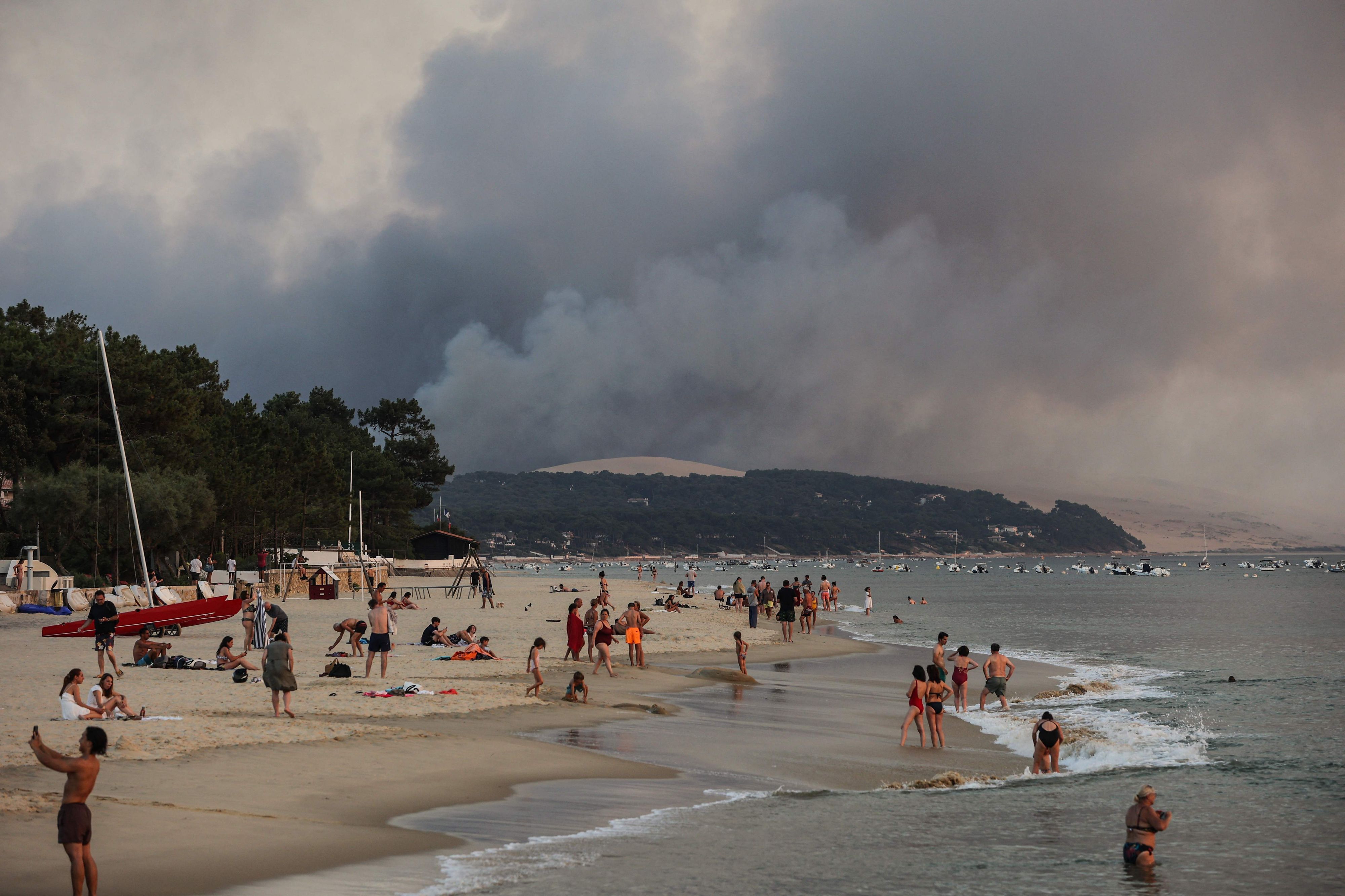 Download von www.picturedesk.com am 24.07.2022 (09:50).  This photograph taken on July 18, 2022 shows people swim on the Moulleau's beach as the smoke rising from the forest fire in La Teste-de-Buch, seen from Arcachon, in front of the Pilat dune. - In scorching heat, with more than 40°C, some 8,000 people had to leave - in a "preventive manner" according to the prefecture - the Miquelots and Pyla-sur-Mer, districts of the municipality of La Teste-de-Buch, a town of 28,000 inhabitants where 4,300 hectares of forest went up in smoke. (Photo by THIBAUD MORITZ / AFP) - 20220718_PD8845 - Rechteinfo: Rights Managed (RM) Nur fÃ¼r redaktionelle Nutzung! Werbliche Nutzung erfordert Freigabe: bitte schicken Sie uns eine Anfrage.