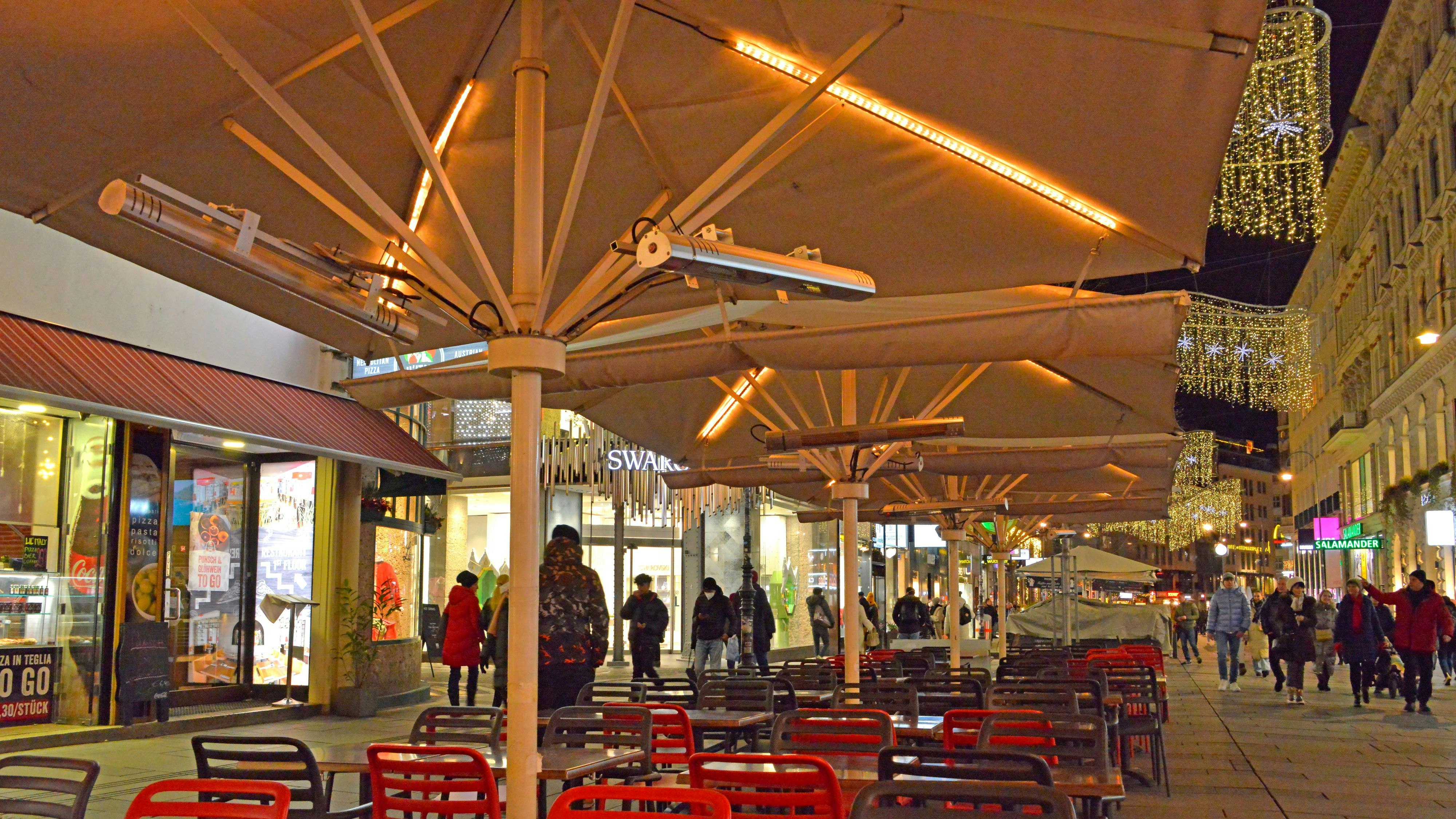 Download von www.picturedesk.com am 25.07.2022 (12:30).  Die Kärntner Straße zur Weihnachtszeit, Nachtaufnahme, Einkaufsstraße, Weihnachtseinkauf, einkaufen, Geschäftsstraße, Winter, Weihnachten, 1. Bezirk, Innere Stadt, 1010, Wien, Österreich, Abendaufnahme. Viele Leute gehen einkaufen oder spazieren, die Geschäfte sind weihnachtlich geschmückt. Ein leerer Gastgarten mit Schirmen im Vordergrund . - 20211220_PD7686 - Rechteinfo: Rights Managed (RM)