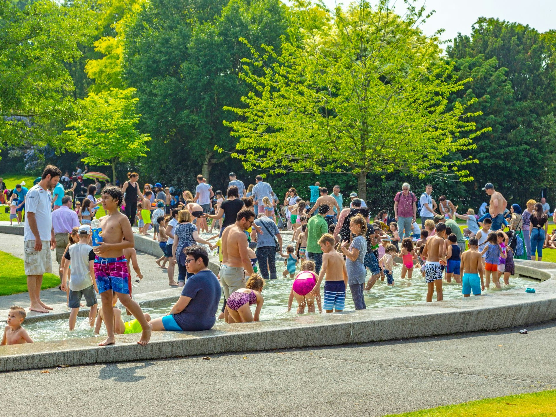 Princess Diana Spencer memorial in Hyde Park with large numbers of people in the water and sitting around the edge during the 2019 heat wave in London.