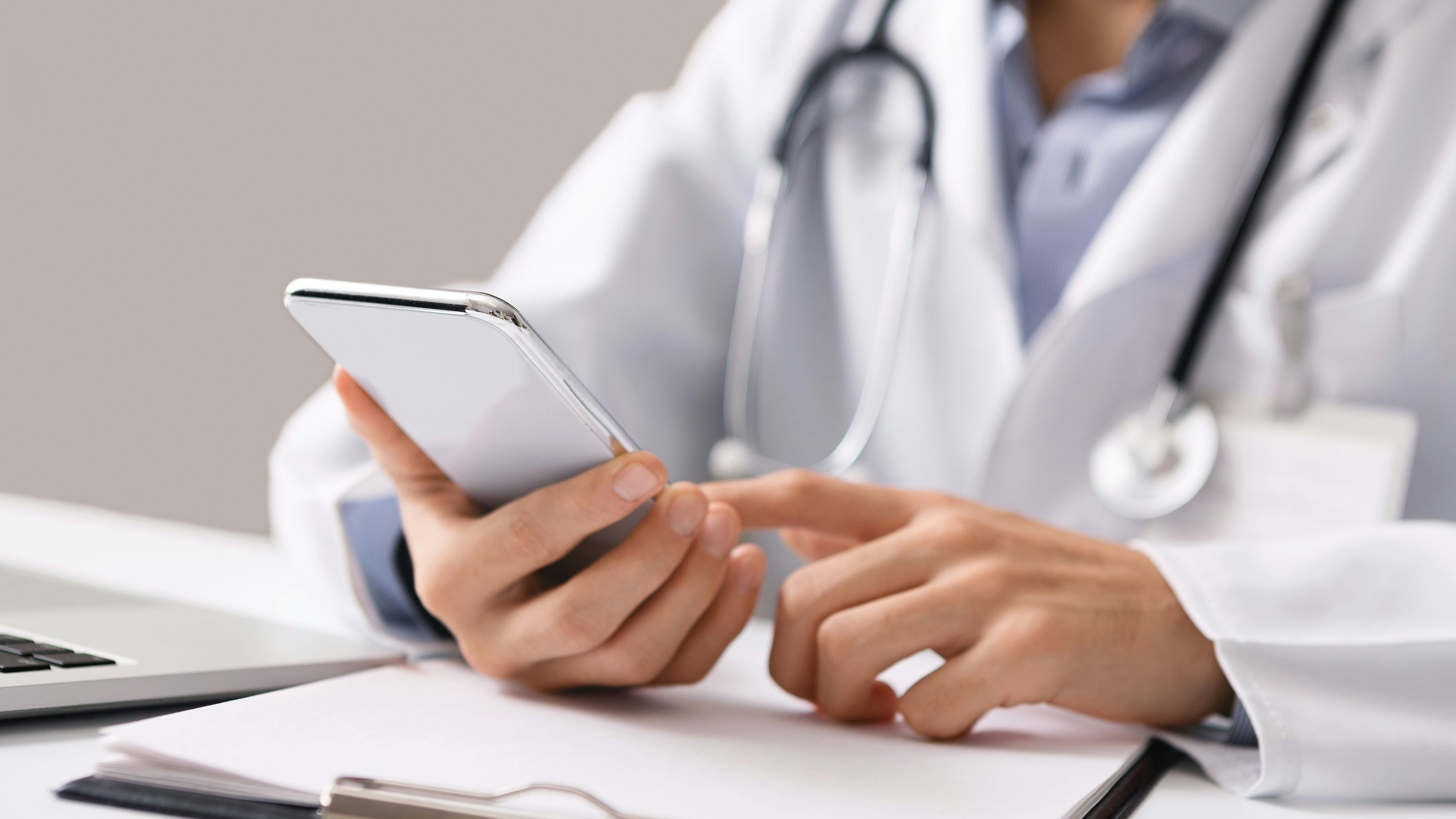 Consultation Online. Unrecognizable male doctor using smartphone at workplace, messaging with his patient, prescribing treatment