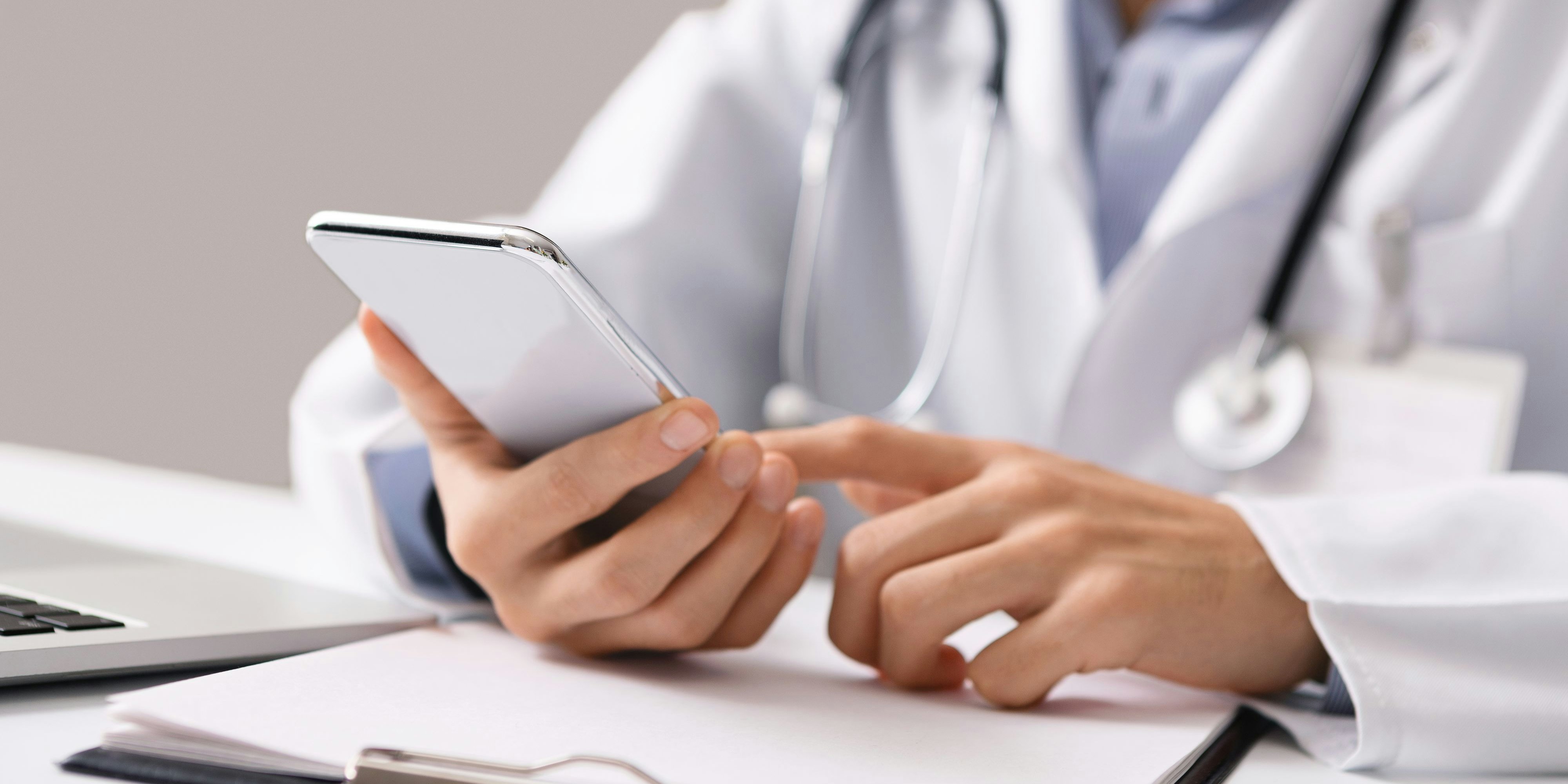 Consultation Online. Unrecognizable male doctor using smartphone at workplace, messaging with his patient, prescribing treatment