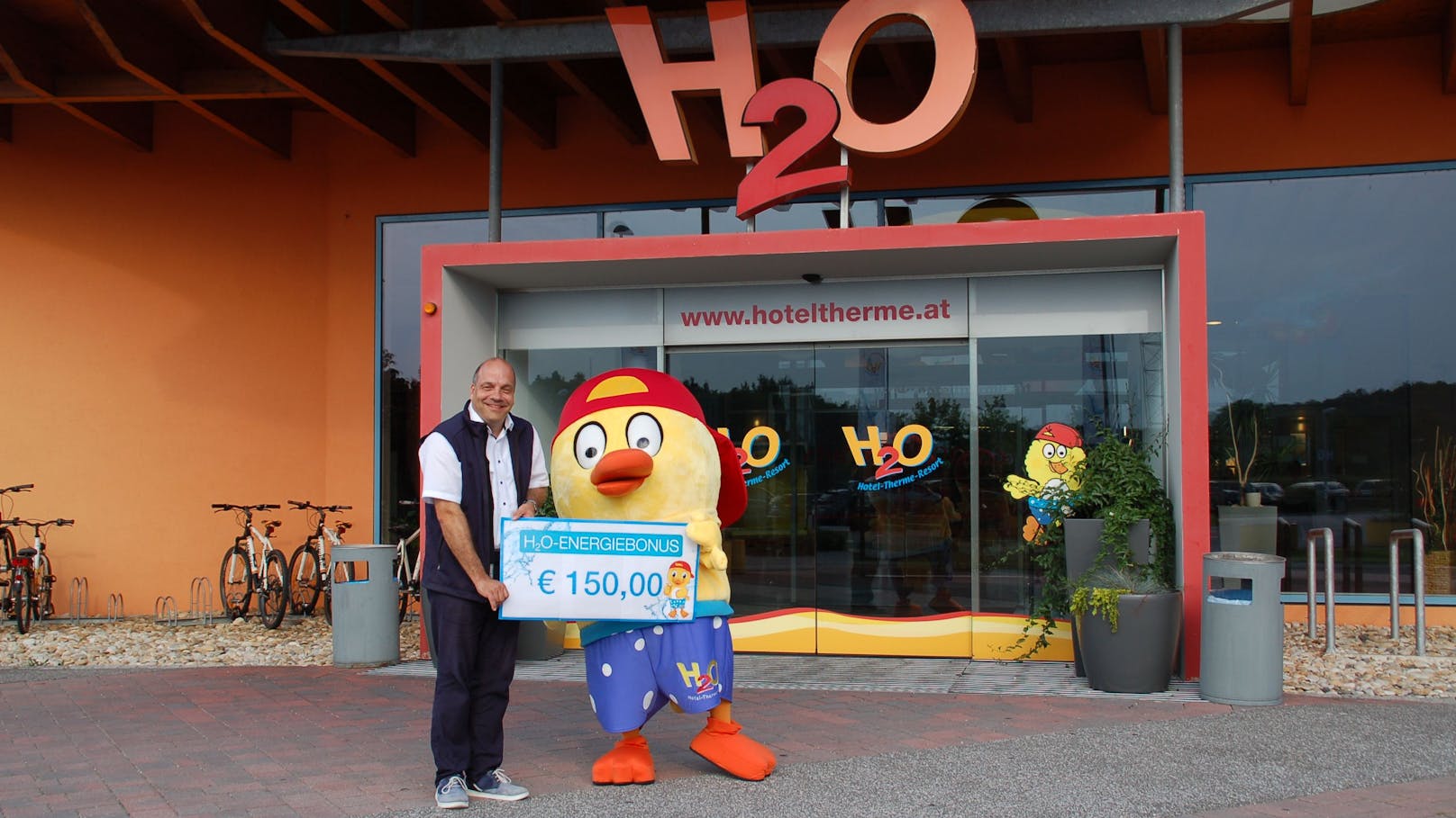 H2O-Therme-Geschäftsführer Christian Rotter und Maskottchen HopiHo überreichen symbolisch den Energiebonus an die Mitarbeiter.