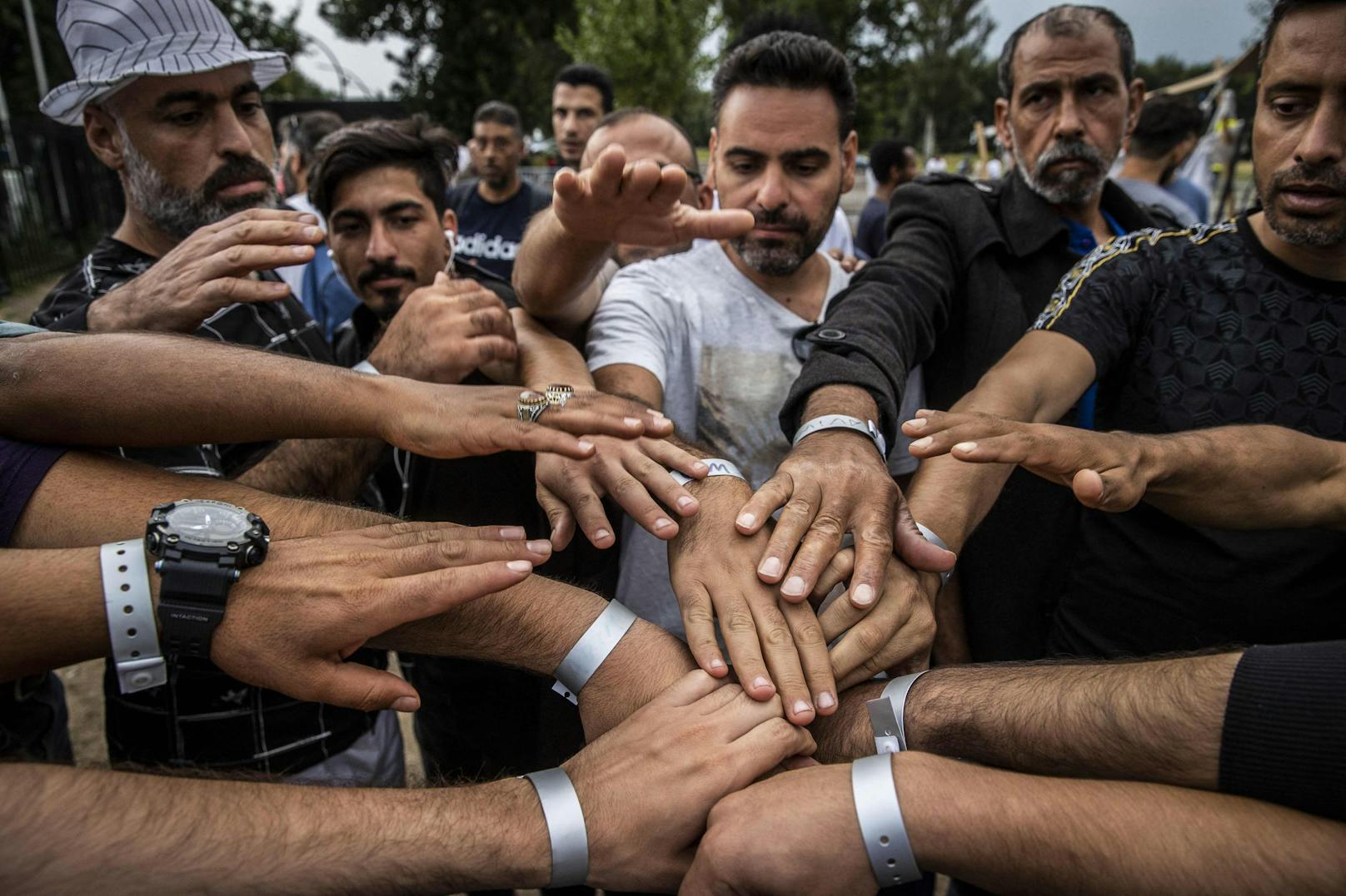 15.08.22: Asylsuchende zeigen ihre farbigen Armbänder, die ihren offiziellen Status im Asylverfahren belegen.
