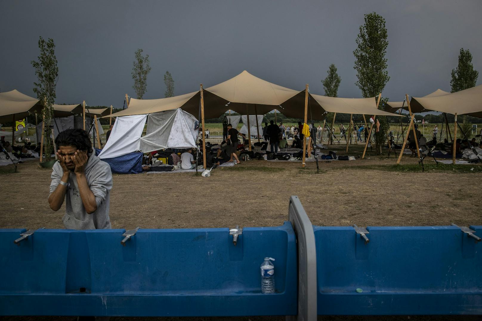 15.08.22: Asylbewerber in ihrer provisorischen Unterkunft vor dem Tor des COA-Asylbewerberzentrums, als sich ein Gewitter entwickelt.