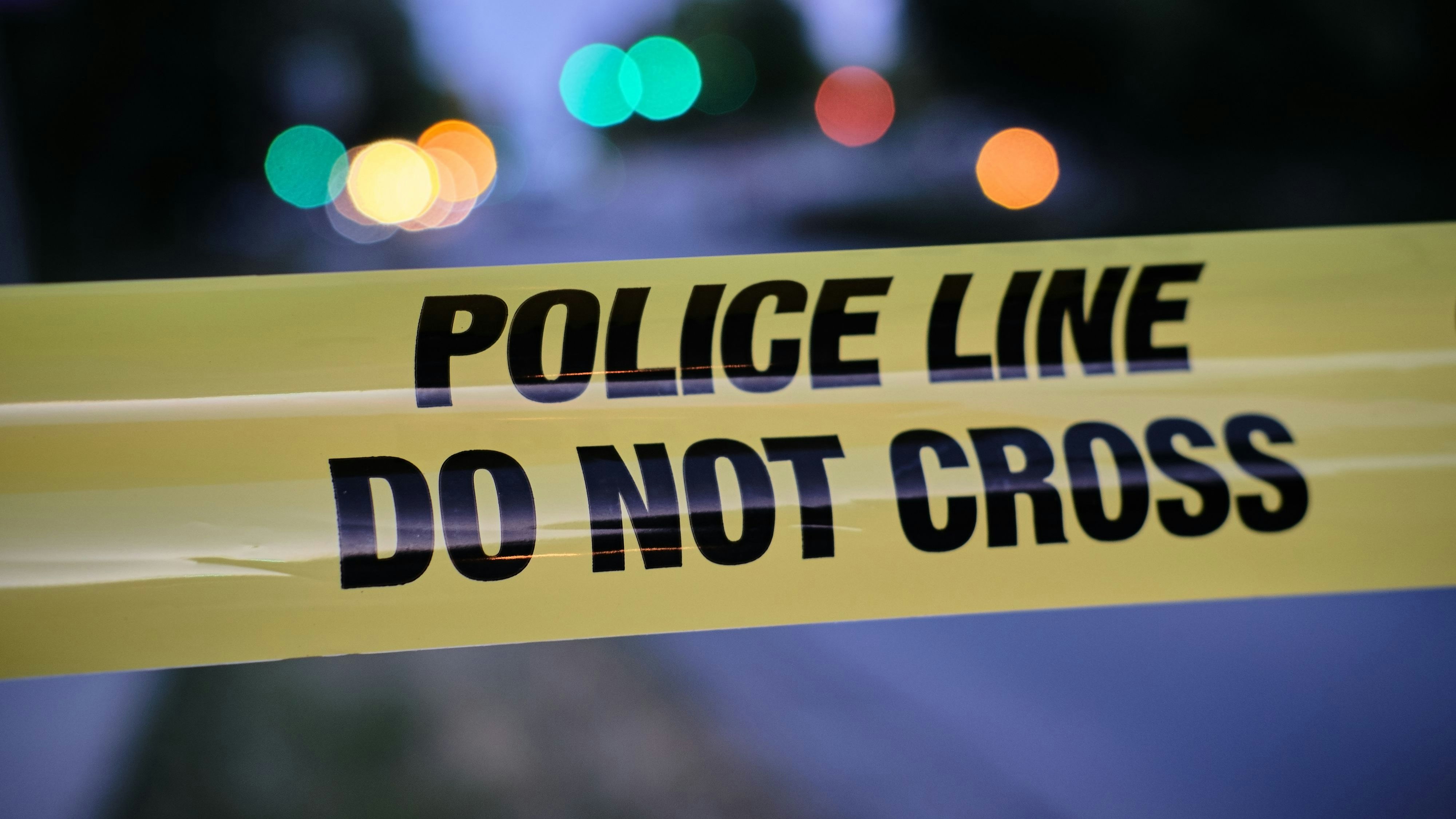 Police yellow line, blurred lights and traffic accident in background.