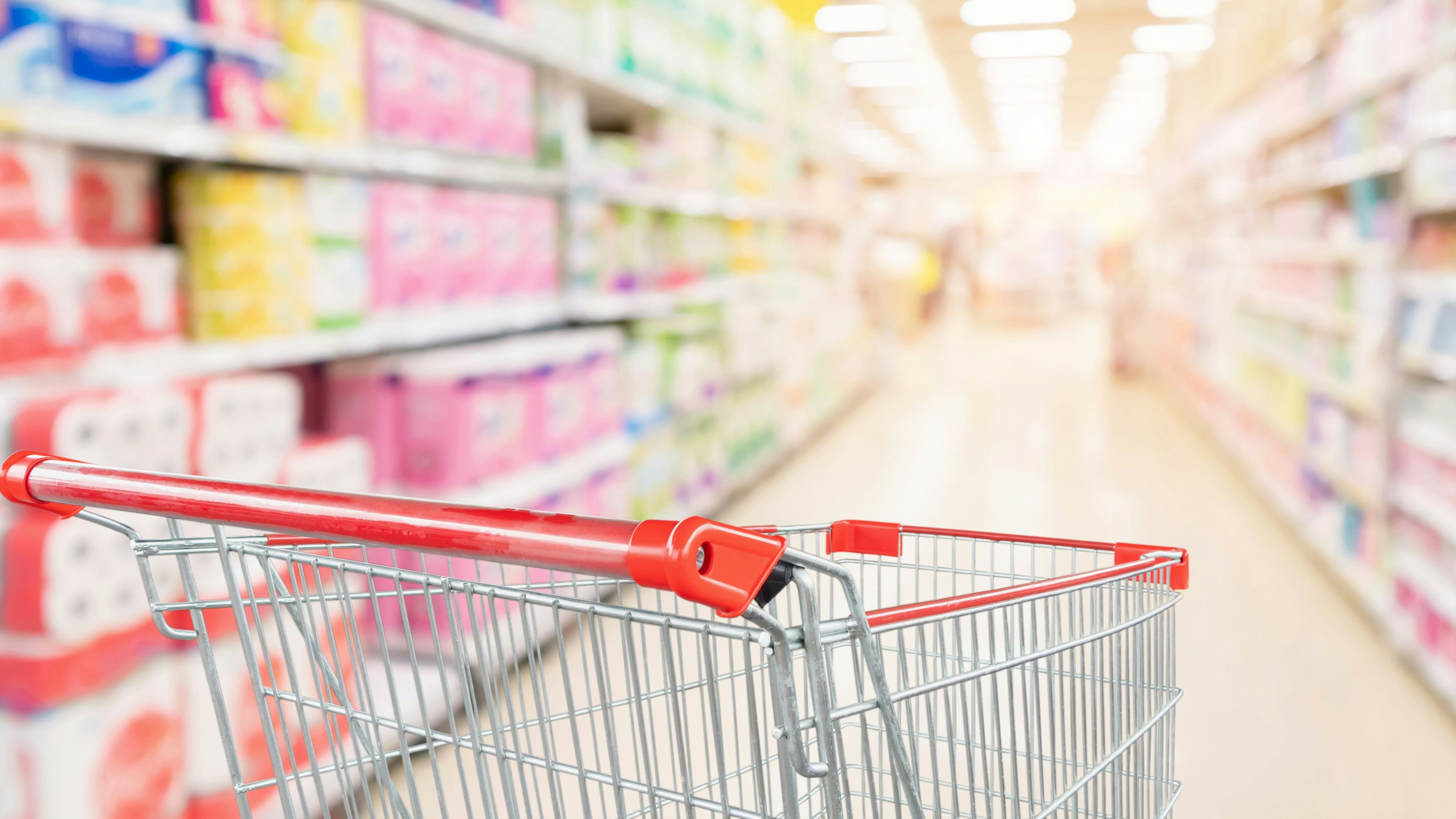 Empty shopping cart with abstract blur supermarket discount store aisle and toilet tissue paper display product shelves interior defocused background