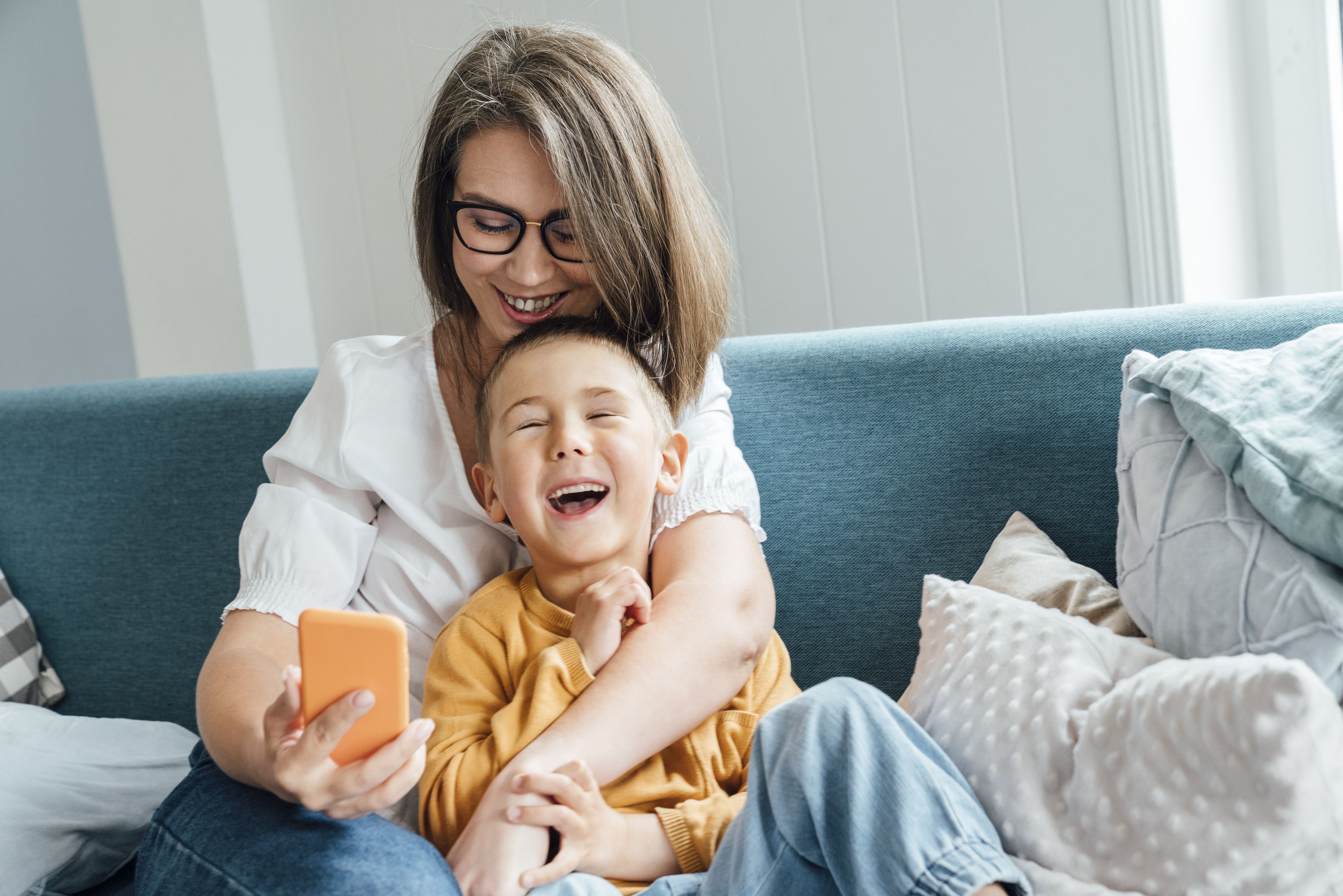 Download von www.picturedesk.com am 26.08.2022 (11:04).  Happy boy with mother holding smart phone sitting on sofa at home - 20220609_PD22005 - Rechteinfo: Royalty Free (RF) Model Released