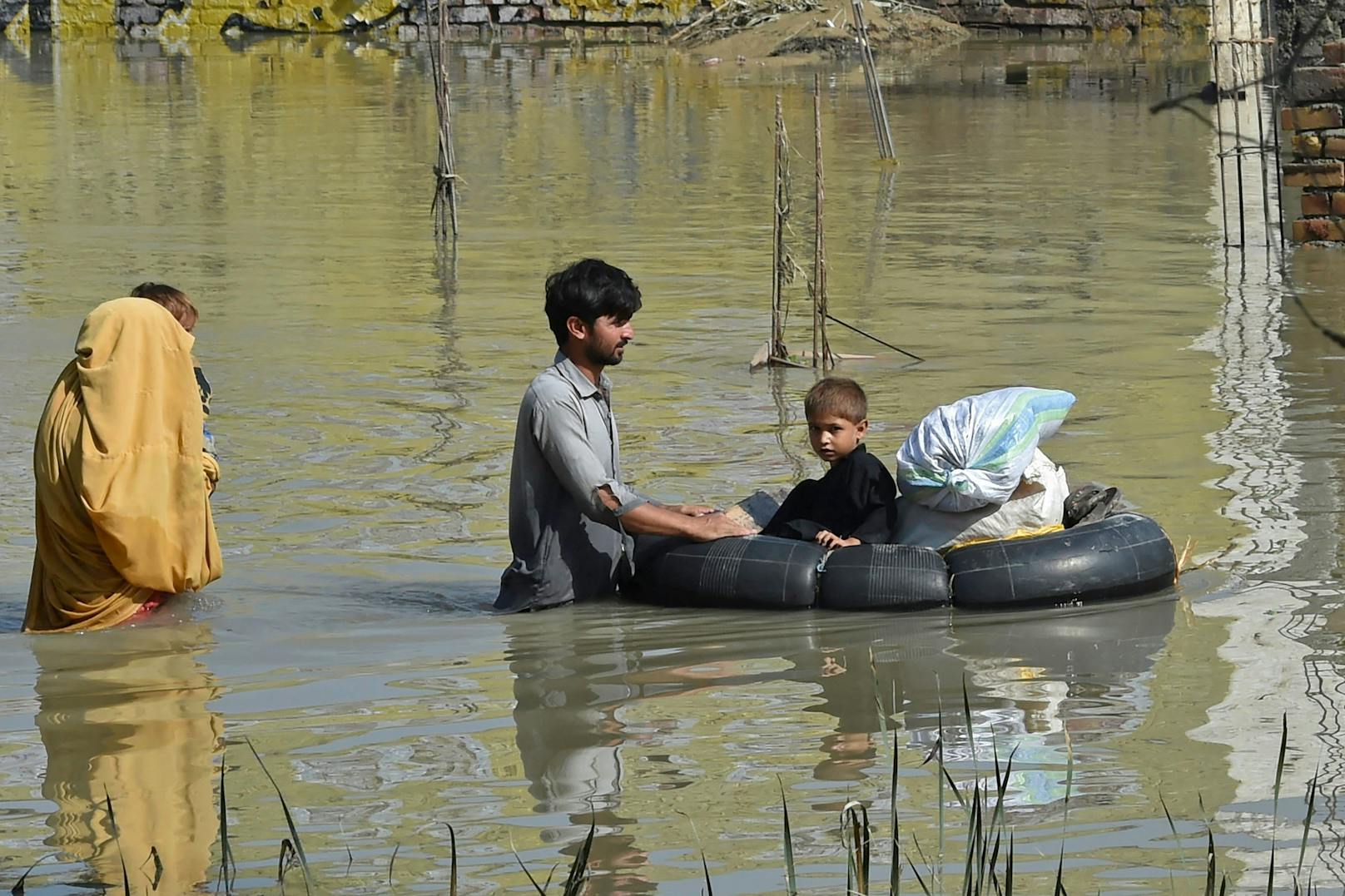 Eine Familie watet nach heftigen Monsunregenfällen im Bezirk Charsadda in Khyber Pakhtunkhwa am 29. August 2022 durch ein von Überschwemmungen heimgesuchtes Gebiet.