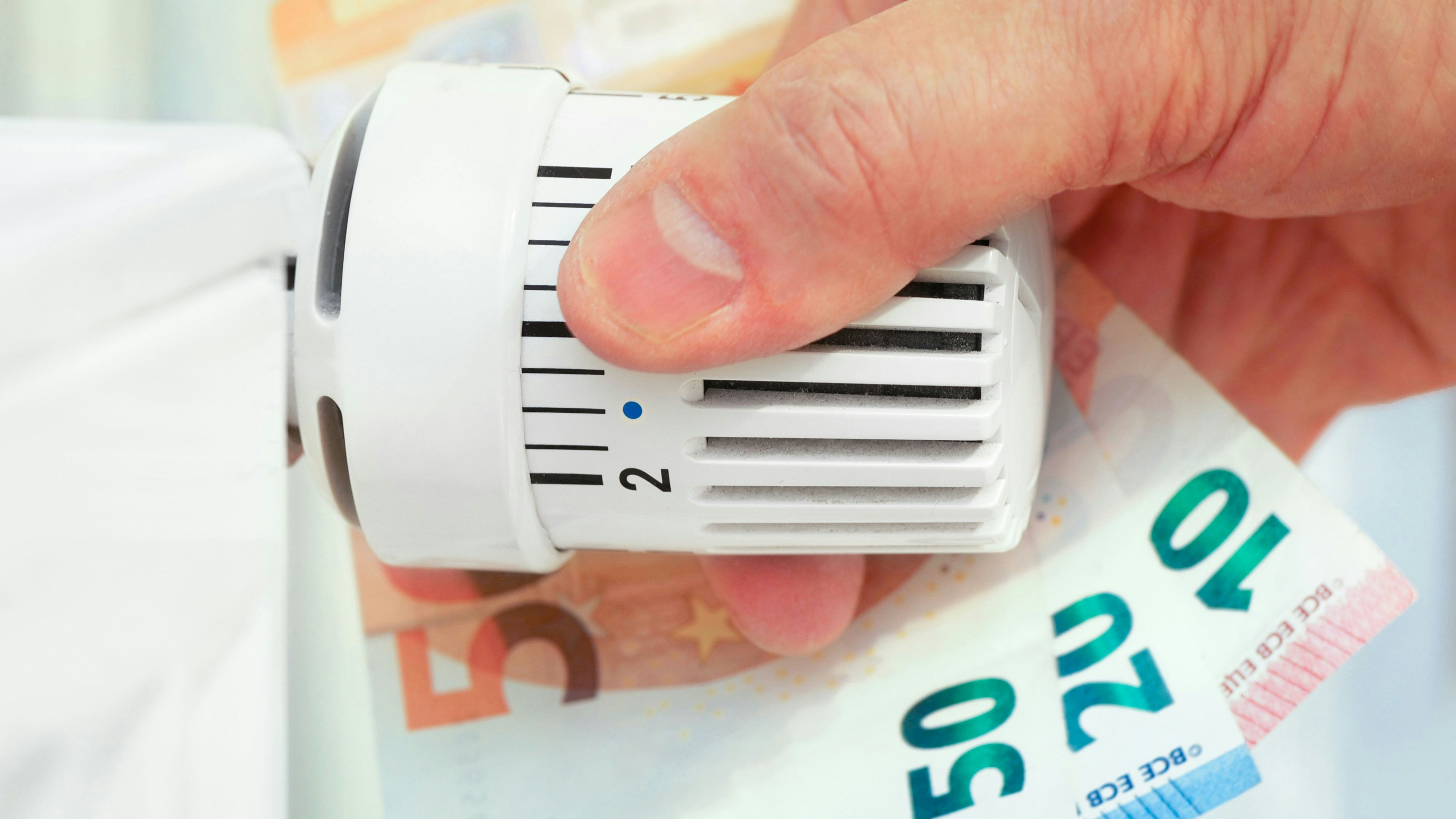 Hand on the heating thermostat with money bills, heating costs concept