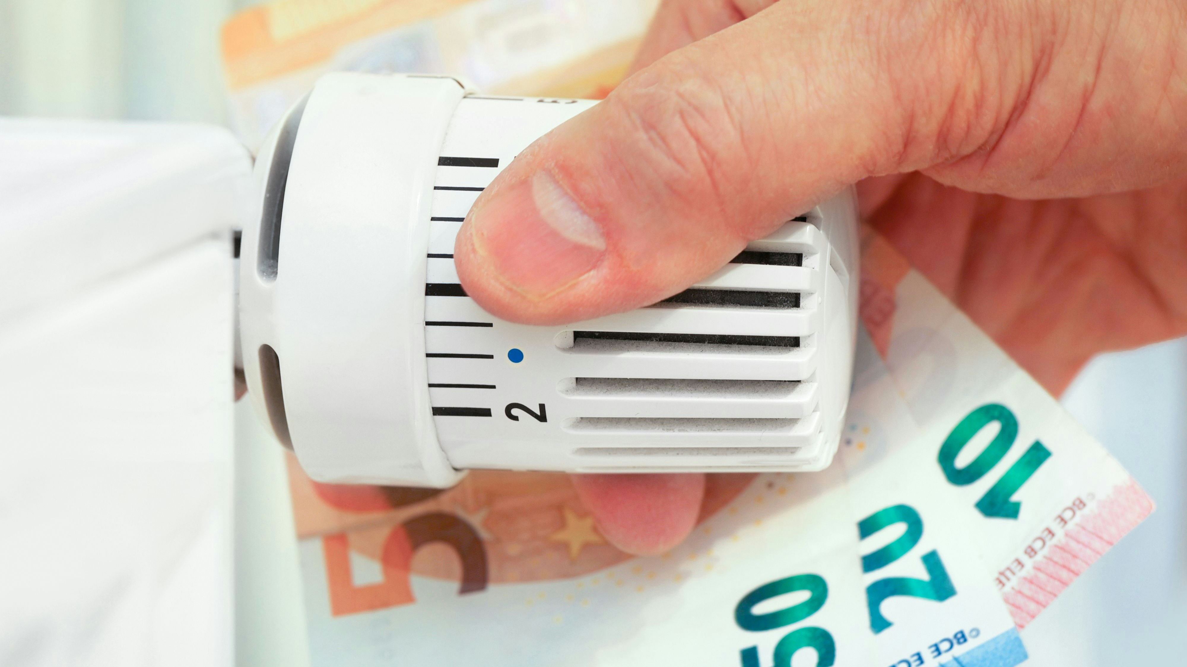 Hand on the heating thermostat with money bills, heating costs concept